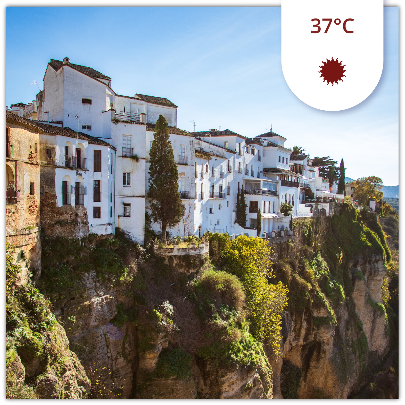 Ilustracja przedstawia białe, stare kamieniczki leżące na skarpie na skraju wąwozu. Niebo jest błękitne. Kamieniczki oświetlane są przez promienie słońca. Na ilustracji znajduje się informacja dotycząca temperatury - trzydzieści siedem stopni Celsjusza. Pod nią znajduje się rysunek słońca. 