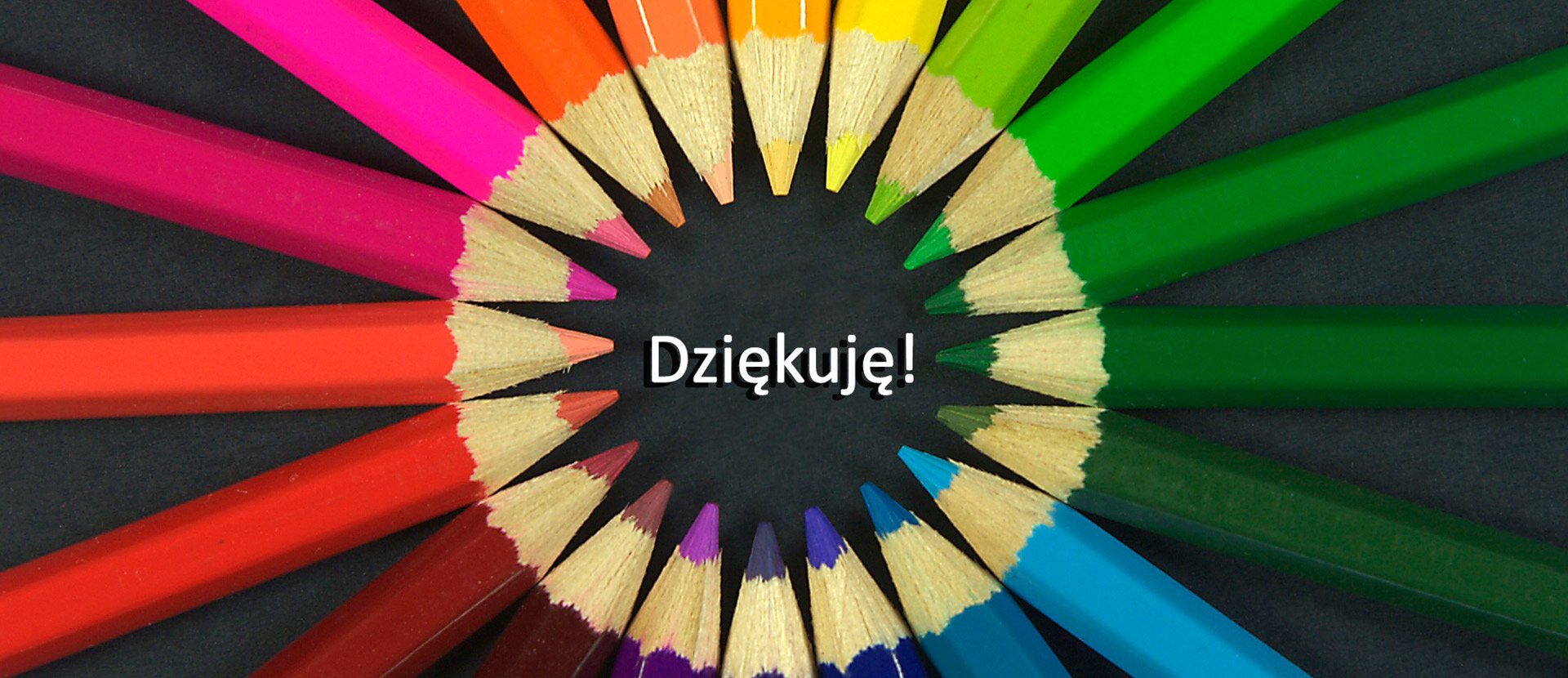 Fotografia przedstawia różnokolorowe kredki ułożone rysikami do środka w kształt okręgu. W wolnej przestrzeni między kredkami widnieje napis "Dziękuję!".