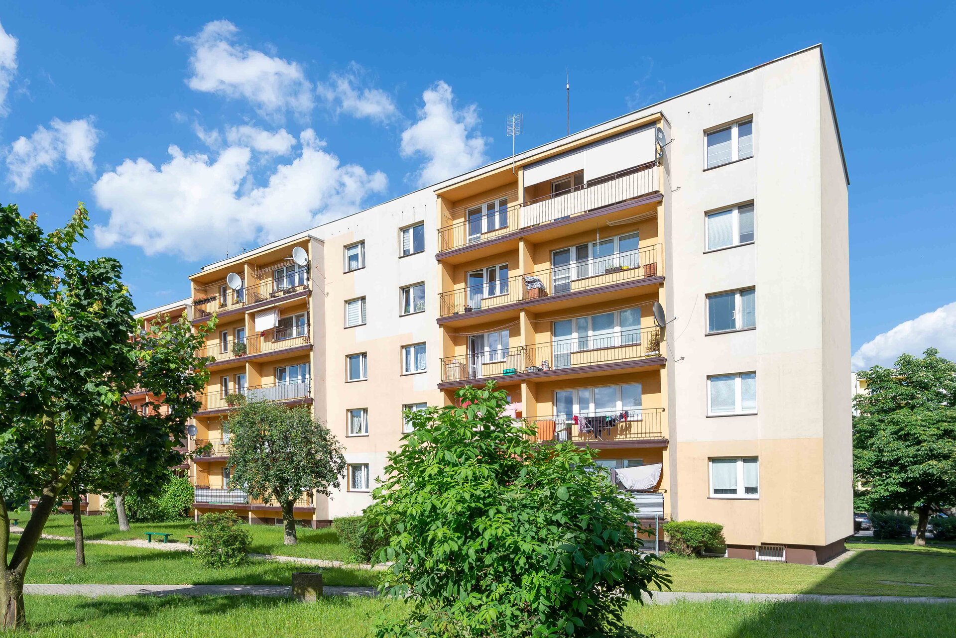 Zdjęcie przedstawia czteropiętrowy blok mieszkalny z balkonami i standardowymi oknami.