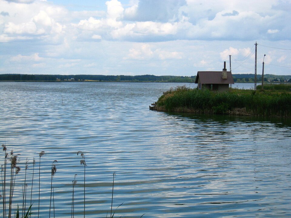 Na zdjęciu jest jezioro. Po prawej stronie fotografii jest brzeg jeziora, stoi na nim mały dom. 