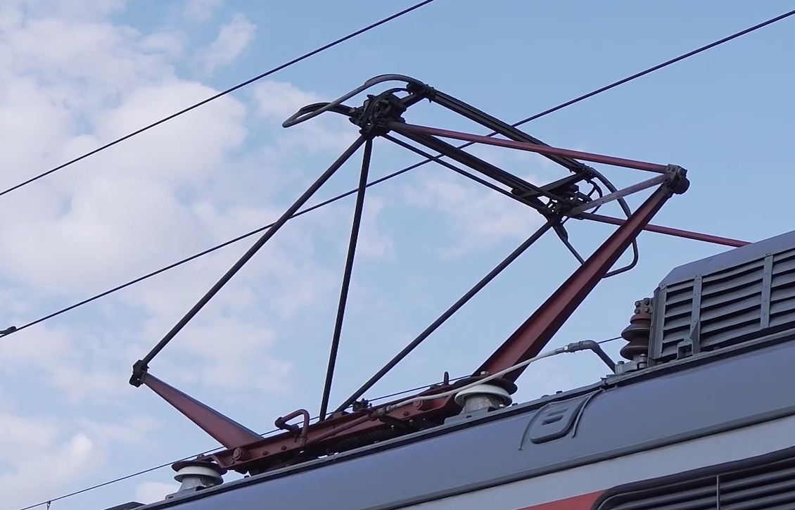 Zdjęcie pokazuje odbierak prądu, inaczej pantograf. Urządzenie ma ramę w kształcie rombu, który odpowiednio wydłuża się lub skraca podnosząc lub opuszczając powierzchnię styków, tak aby zetknąć ją z przewodem jezdnym widocznym powyżej. 