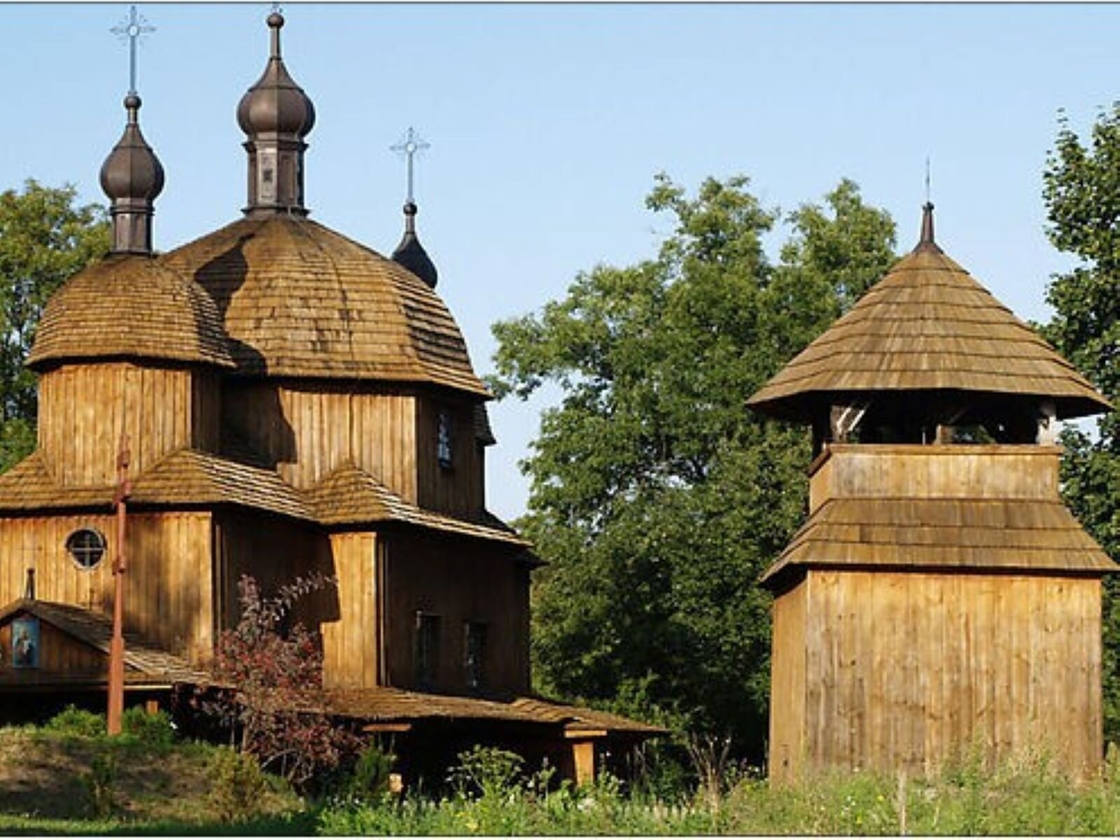Zdjęcie przedstawia drewnianą cerkiew i dzwonnicę w Muzeum Wsi Lubelskiej w Lublinie. 