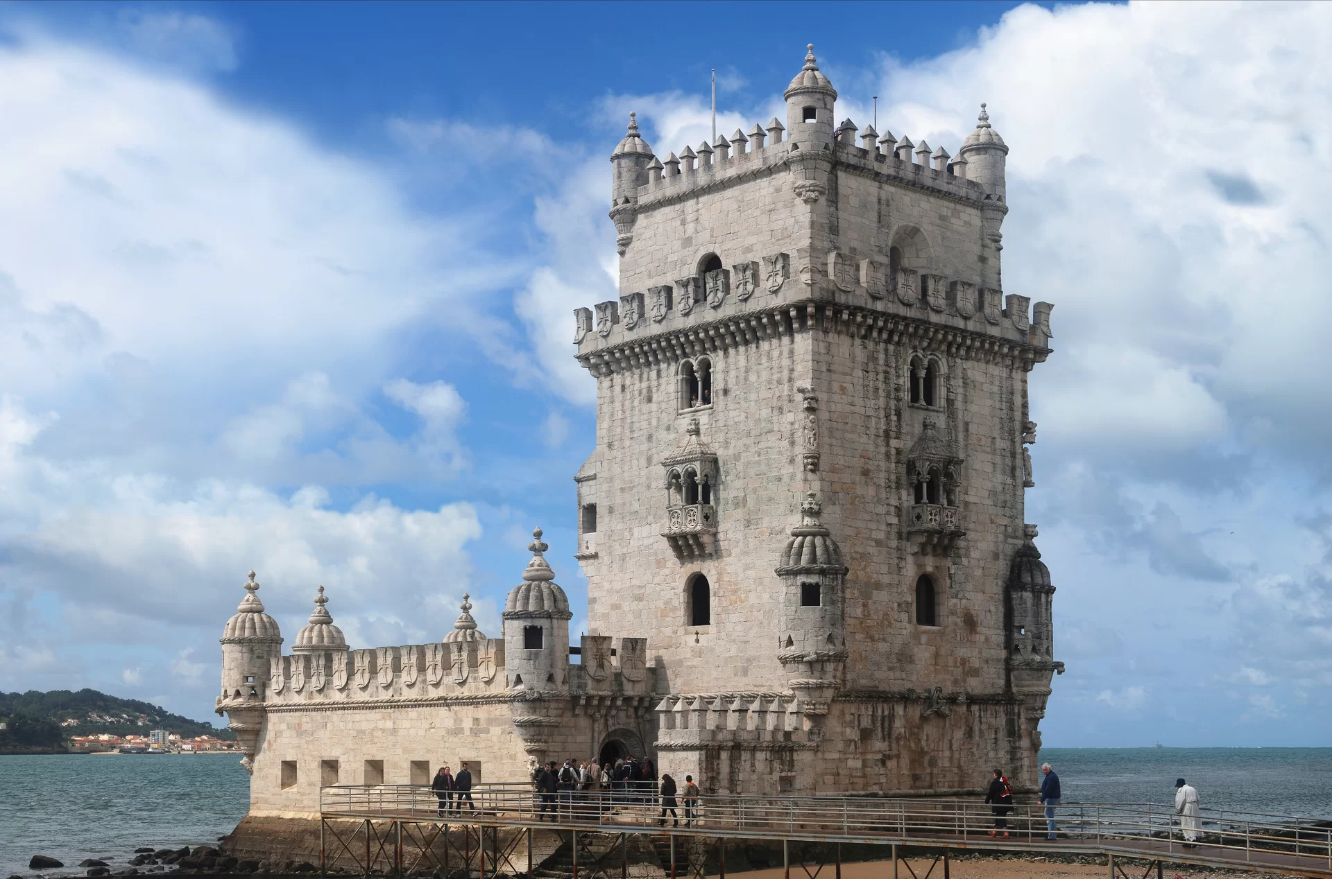 Na ilustracji budowla, która składa się z dwóch części: z bastionu (z lewej) oraz z wieży (z prawej). Bastion posiada nisko sklepioną kaplicę ze strzelnicami dla armat. Materiały użyte do budowy, widoczne na zdjęciu, to głównie kamień wapienny (marmur) i cegła. Dekoracje zainspirowane tematyką wojenną. Wieża składa się z kilku pięter. Środkowe kondygnacje ozdobione są balkonami z małymi zdobionymi kolumnami, widoczne łukowe okna, na rogach wieży okienka strzelnicze. Jedno z pięter otoczone jest balkonami z półokrągłymi łukami. Zwieńczenie budowli tworzą większe wieże na każdym z narożników oraz mniejsze pomiędzy nimi. Pośrodku znajduje się obniżone patio. Taras jest otoczony balustradą z wieżyczkami i prążkowanymi kopułami. Poniżej wieżyczek dwie rzeźby: Archanioła Michała oraz św. Wincentego (patrona Lizbony). Aby dostać się do wieży trzeba przejść przez most znajdujący się po prawej stronie zdjęcia. Widoczni na nim spacerowicze, przed wejściem kolejka zwiedzających wieżę. Na drugim planie wzniesienie pokryte drzewami, poniżej budynki. Cała wieża stoi przy wodzie, która rozciąga się od lewej do prawej strony zdjęcia.