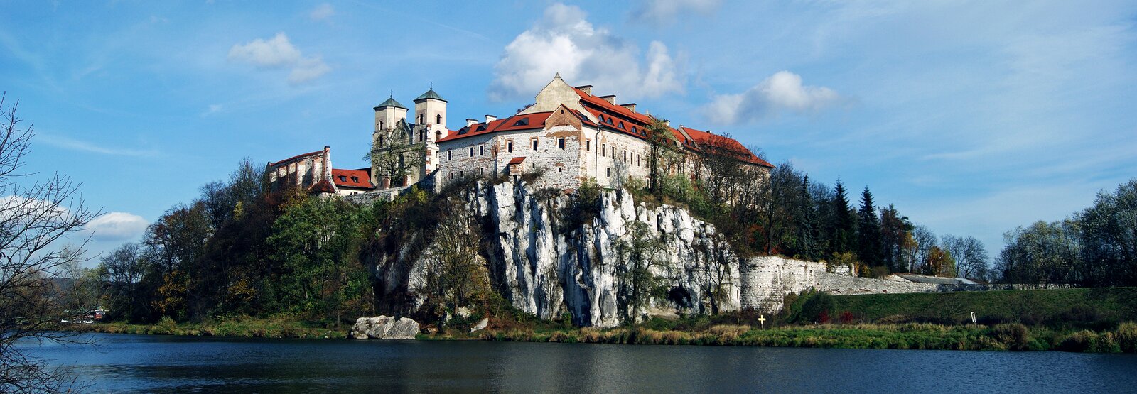 Zdjęcie przedstawia zabudowania z białego kamienia pokryte czerwonym dachem na skalnej skarpie nad rzeką. Budynki otoczone są murami obronnymi, jednym z budynków jest kościół o dwóch wieżach.