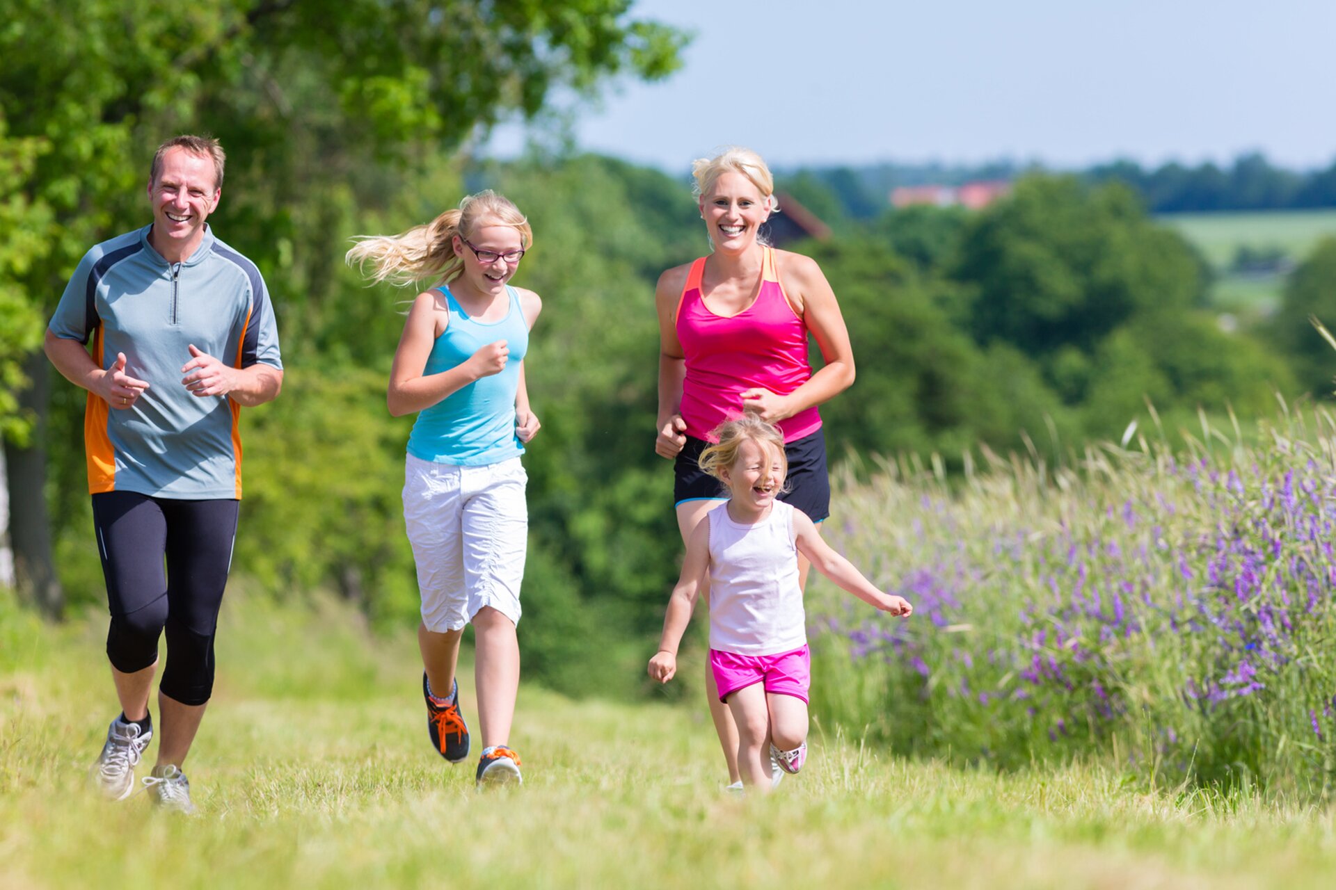 Rodzina uprawiająca biegi na świeżym powietrzu. Na fotografii widoczni biegnący rodzice, a pomiędzy nimi dwie dziewczynki, wysoka strasz i niska młodsza.