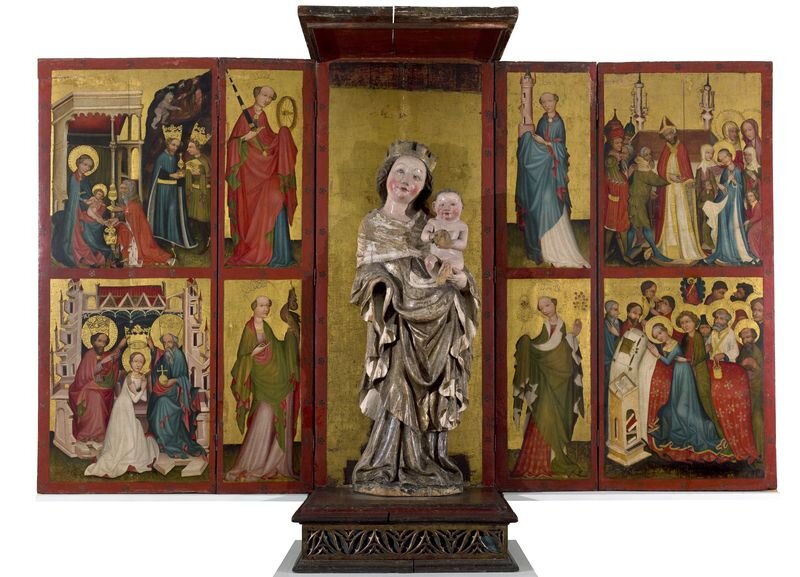 Zdjęcie przedstawia dwuskrzydłowy ołtarz. W jego centralnej części na drewnianym podeście stoi rzeźba Matki Boskiej trzymającej na rękach nagie niemowlę, Jezusa. Kobieta ubrana jest w powłóczystą szatę, na głowie ma koronę. Na obu skrzydłach ołtarza znajdują się sceny z życia Chrystusa oraz postacie świętych.