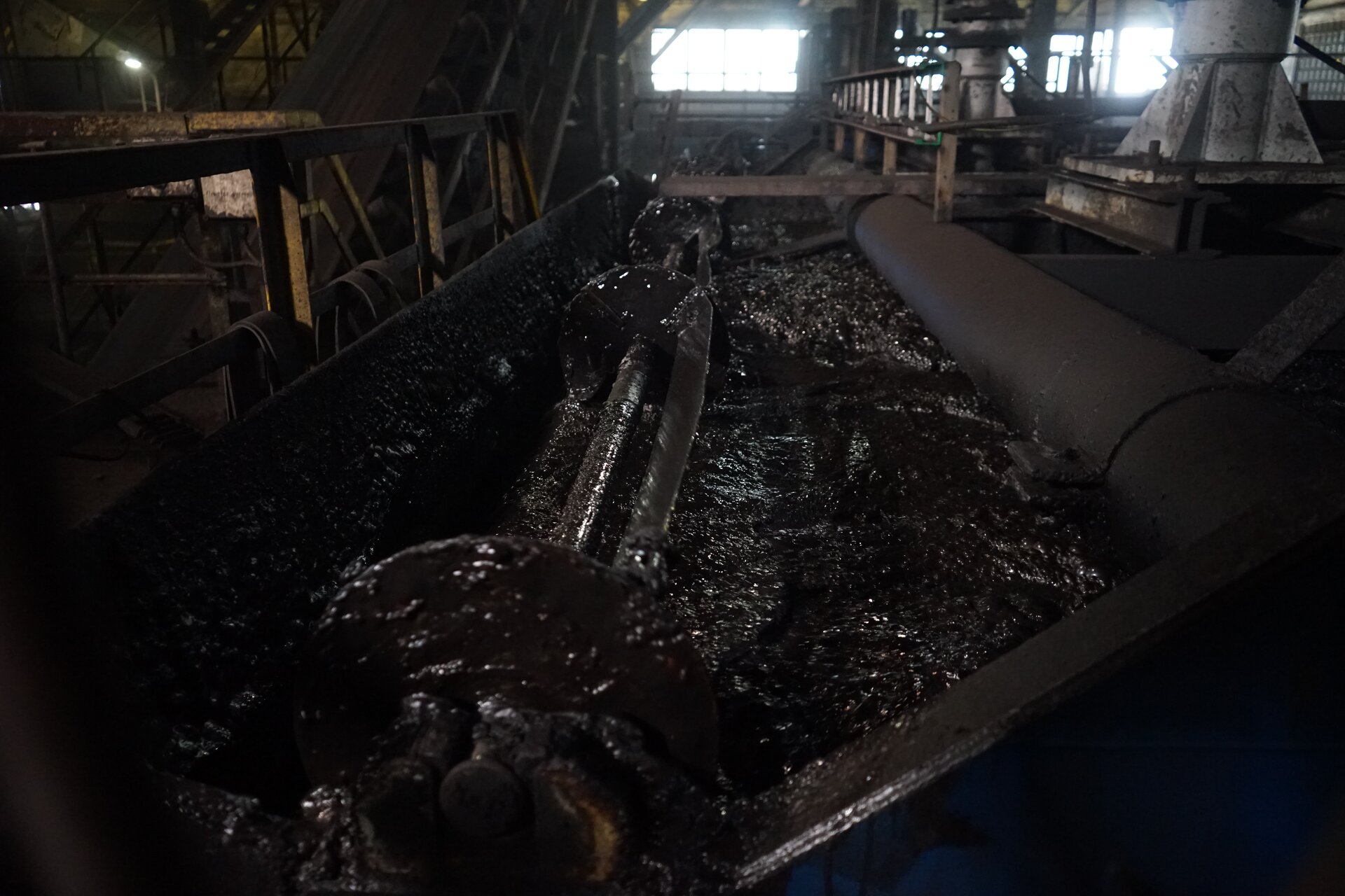 Zdjęcie przedstawia zgarniacze skrzydełkowe wraz z pianą flotacyjną utworzoną we wnętrzu flotownika podczas wzbogacania węgla surowego. Zgarniacz skrzydełkowy znajduje się na środku. Łopatki zamocowane na zgarniaczu oblepione są pianą pokrytą czarnymi ziarnami węgla. Piana wydaje się gęsta oraz lepka wypełnia całą komorę. Zgarniacz jest zamontowany tuż przed korytem odbiorczym flotownika. i znajduje się nieco poniżej poziomu cieczy. Zgarniacze skrzydełkowe stanowią usytuowane poziomo, równolegle do poziomu koryta odbiorczego trzony obracające się w trakcie pracy urządzenia wokół własnej osi. Wokół trzonów rozmieszczone są promieniście, dookoła wspomnianej osi, na całej ich długości płaskie, prostokątne elementy, czyli skrzydełka, tudzież łopatki. Zgarniacz odpowiada za wynoszenie piany bogatej w koncentrat poza maszynę flotacyjną. Poniżej zdjęcia znajduje się przycisk multimedialny z nagraniem audio. Treść nagrania jest zgodna z tytułem zdjęcia.