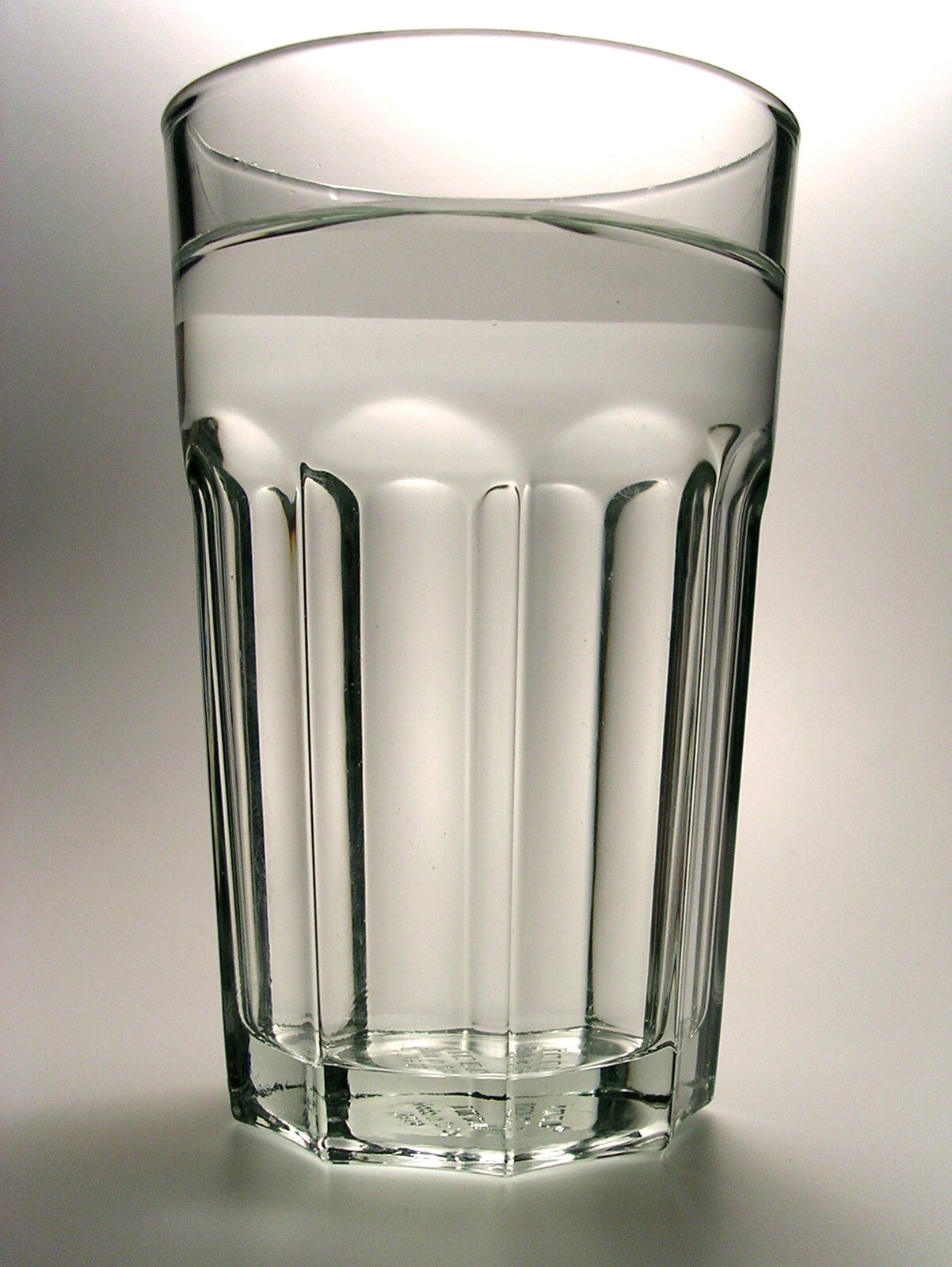 Zdjęcie przedstawia szklankę wypełnioną wodą stojącą na szarym tle.