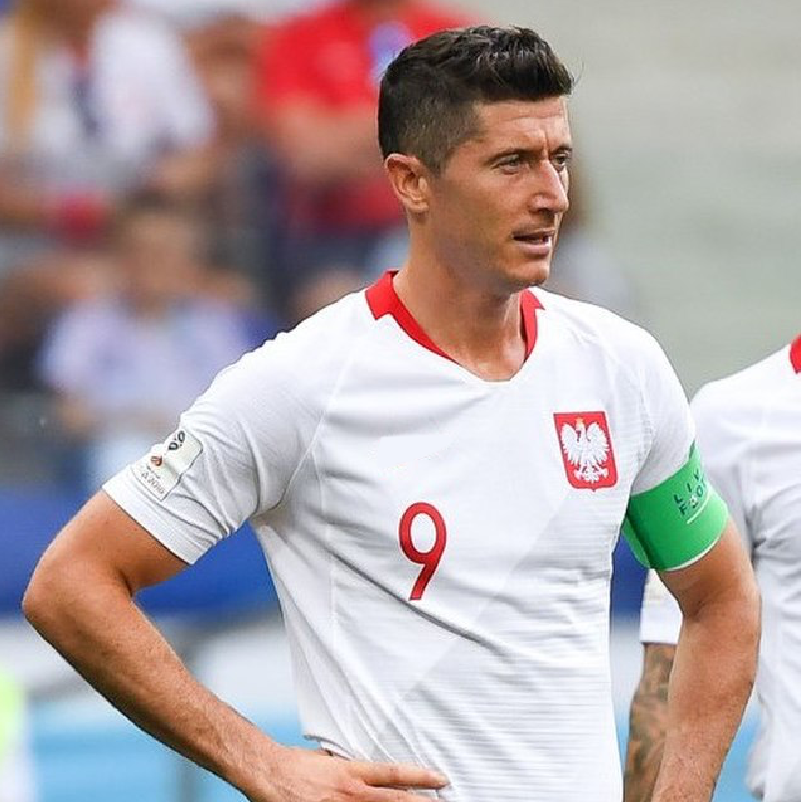 Zdjęcie przedstawia Roberta Lewandowskiego w białej koszulce polskiej reprezentacji, z godłem i numerem dziewiątym. 
