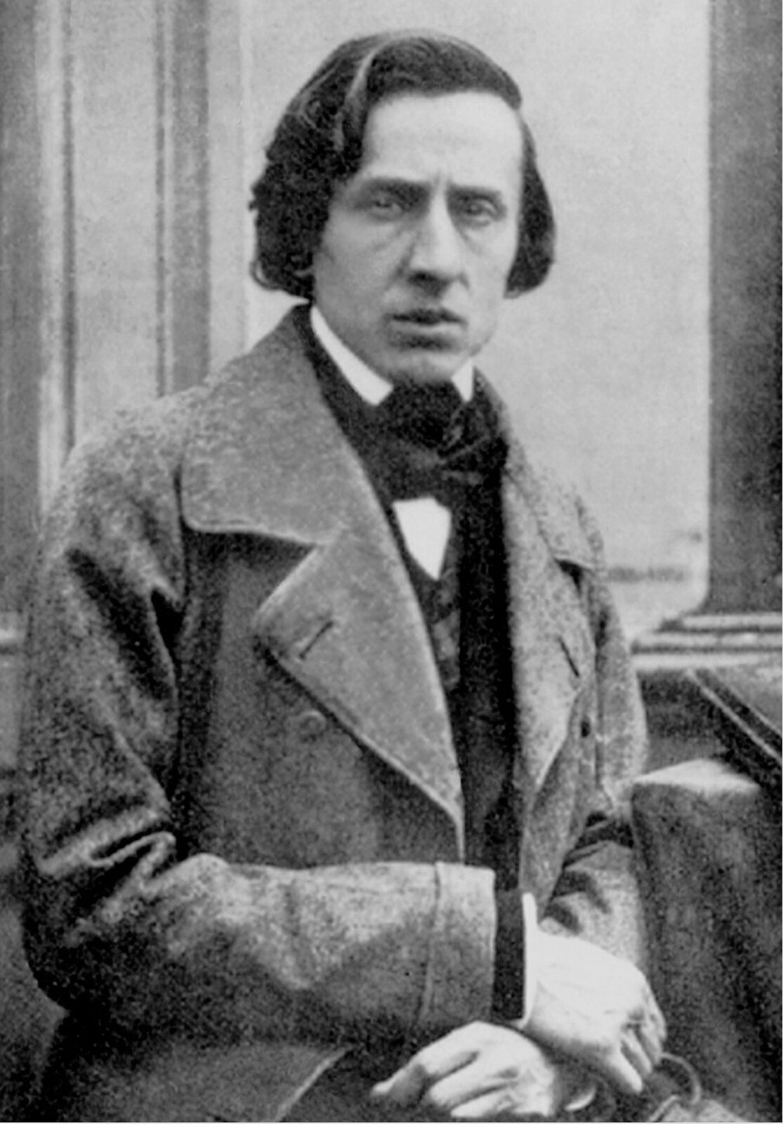Na fotografii Fryderyk Chopin. Kompozytor siedzi, ręce ma skrzyżowane na udach. Patrzy na wprost. Ma dłuższe, ciemne włosy, zakrywające ucho. Niewielkie ciemne oczy, dość wyraźne brwi. Duży nos i średnie usta. Jest smutny, bądź zamyślony. Ubrany jest w białą koszulę i jasny płaszcz. Pod szyją ma zawiązaną ciemną apaszkę. Fotografia jest czarno‑biała.