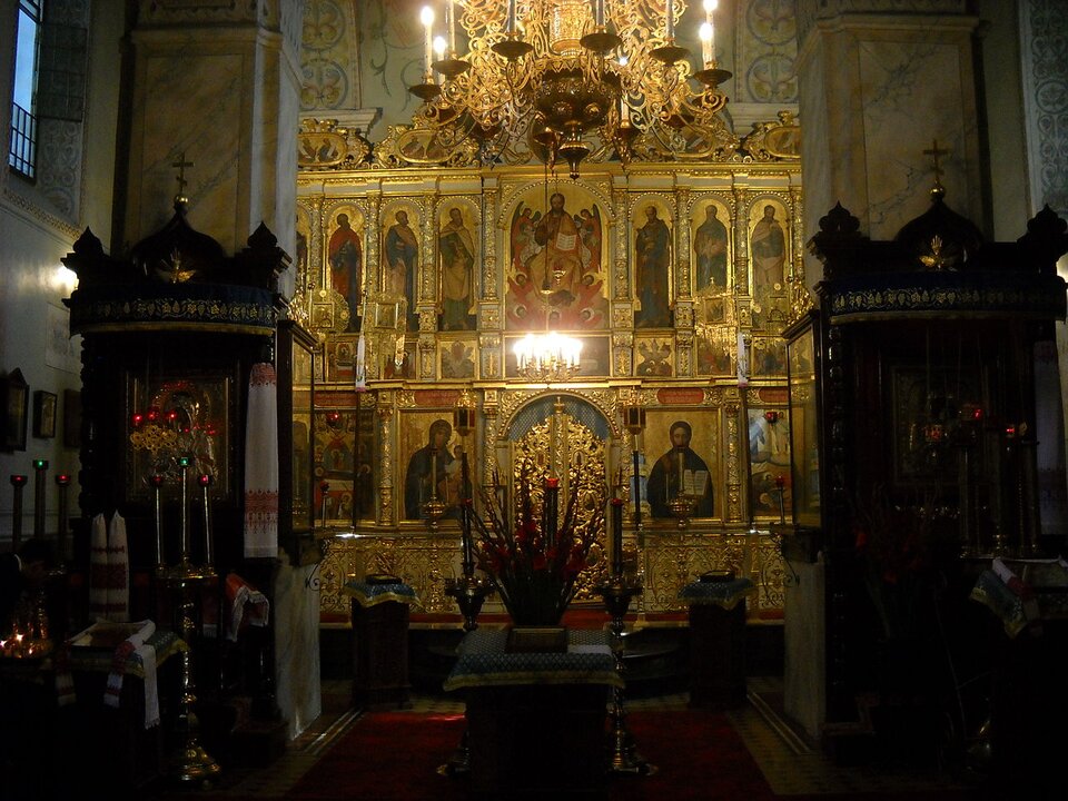 Ilustracja przedstawia wnętrze świątyni prawosławnej. Ukazany został złoty, ozdobny ołtarz z wizerunkami świętych. Na środku sklepienia wisi złoty żyrandol. Po bokach głównego ołtarza widoczne są dwa mniejsze boczne ołtarze, wykonane z ciemnego drewna.  