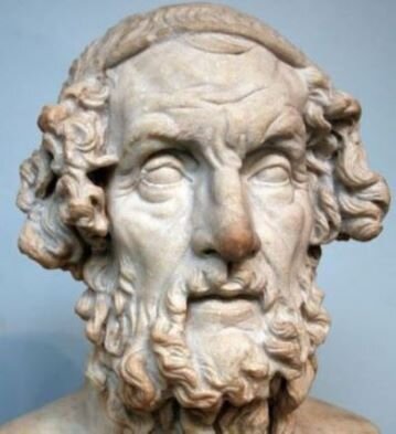 Ilustracja przedstawia rzeźbę głowy starego mężczyzny. Ma on kręcone włosy przepasane opaską, brodę oraz wąsy. Ma szczupłą twarz podkrążone oczy, prosty, wydatny nos.