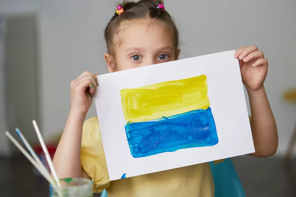 Zdjęcie: dziewczynka trzymająca przed sobą namalowaną farbami flagę Ukrainy.