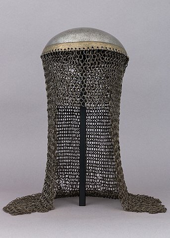 Fotografia barwna przedstawia misiurkę turecką. Jest to rodzaj hełmu, chroniącego głowę przed uderzeniami przeciwnika. Składa się z części metalowej, chroniącej głowę w formie metalowej płaskiej miski i z doczepionego do niego długiego kaptura, zrobionego z metalowych kółek. Kaptur ma 35 cm długości, chroni kark, potylicę, czoło, skronie i ramiona. 