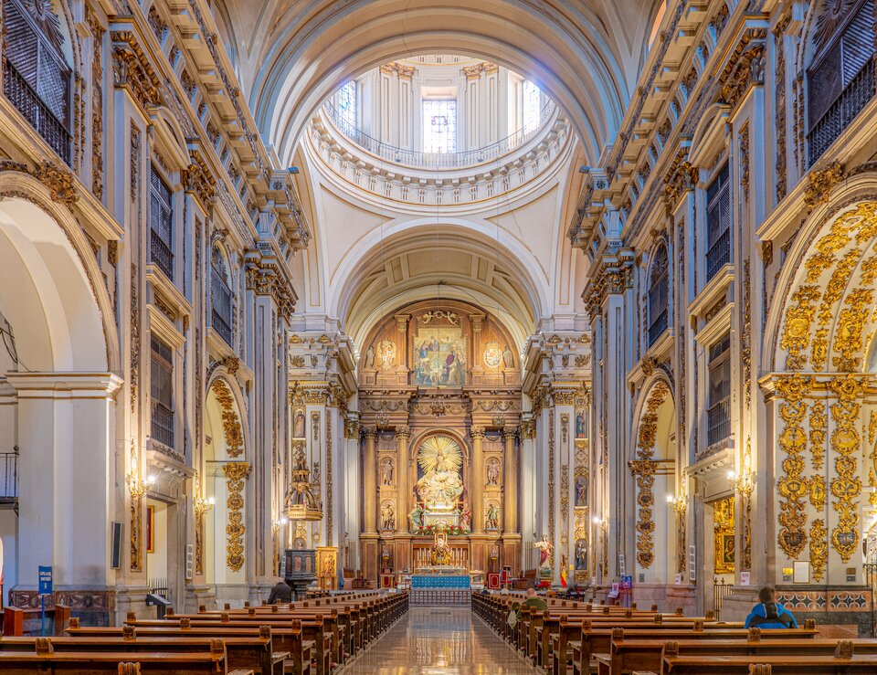 Ilustracja przedstawia wnętrze kościoła San Isidro del Real w Madrycie. Na fotografii znajduje się nawa główna, na końcu której znajduje się ołtarz. Tuż przed prezbiterium z ołtarzem i transeptem, znajdują się łuki międzynawowe, nad którymi widoczny jest fragment kopuły. Nawy boczne są oddzielone od nawy głównej bogato zdobionymi łukami arkadowymi.