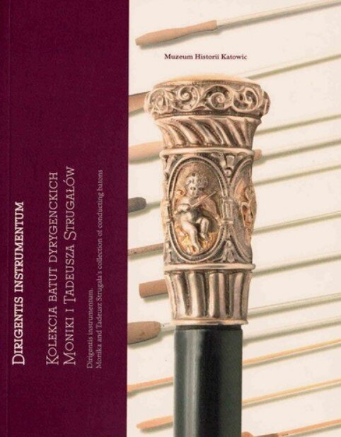 Okładka książki z bordowym paskiem po lewej i zdjęciem po prawej. Na zdjęciu widoczna jest bogato zdobiona głowica batuty dyrygenckiej z reliefem putta (małego aniołka) oraz ornamentami roślinnymi, osadzona na czarnym trzonie. W tle widać inne batuty ułożone poziomo. Na okładce znajdują się napisy w języku polskim, m.in. „Muzeum Historii Katowic” oraz tytuł dotyczący kolekcji batut dyrygenckich Moniki i Tadeusza Strugałów.