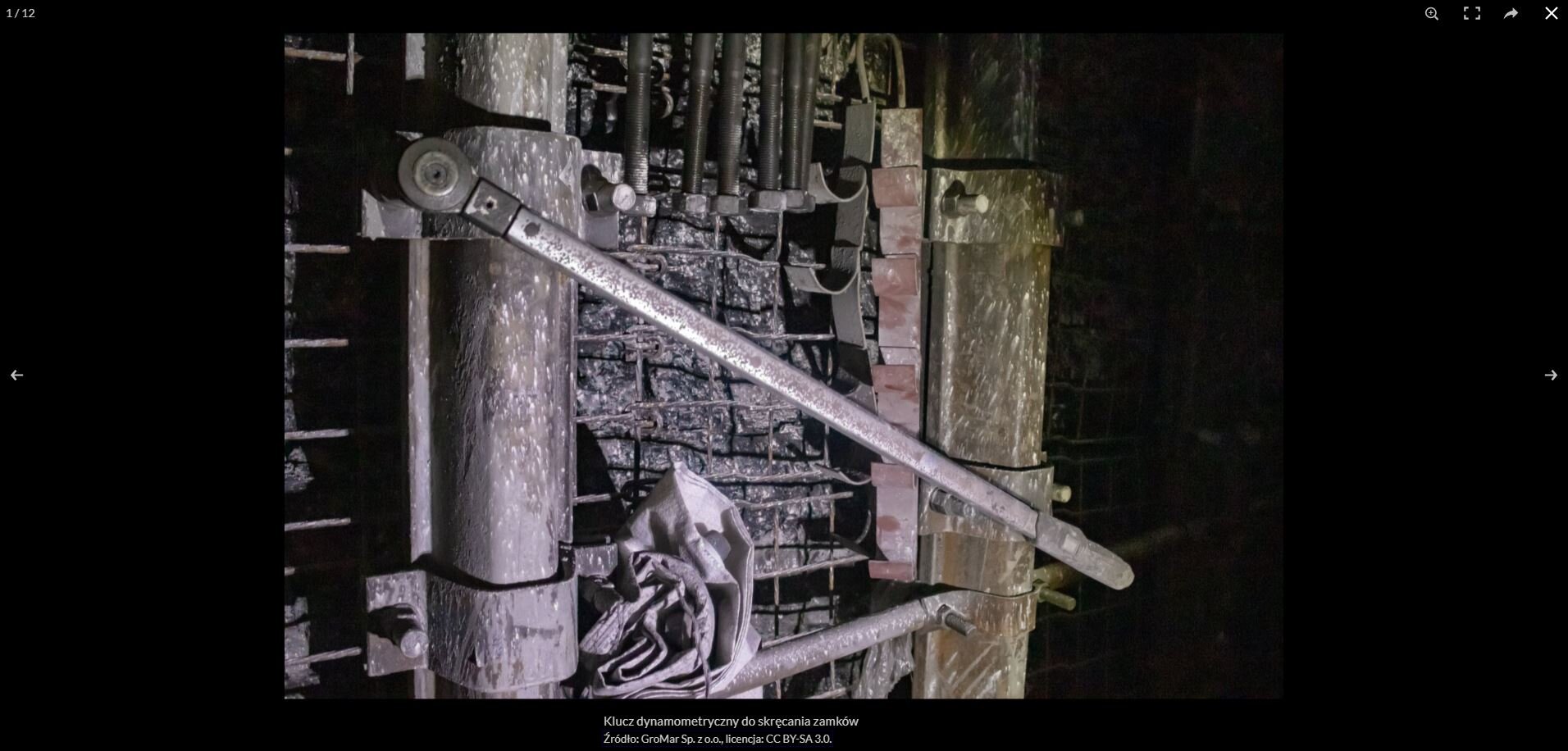 Na zdjęciu widać przykładowe powiększenie zdjęcia z galerii. W centralnej części zdjęcia znajduje się klucz o kształcie zbliżonym do podłużnego cienkiego prostokąta. . Na dole pierwszego zdjęcia od lewej strony znajduje się napis: klucz dynamometryczny do skręcania zamków. Po lewej stronie kucz zakończony jest okrągłą wypustką. Wypustka nałożona jest na śrubę. W tel widać fragment obudowy łukowej. Wyrobiska pomiędzy fragmentami łuków zabezpieczone jest stalową siatką oczkową.