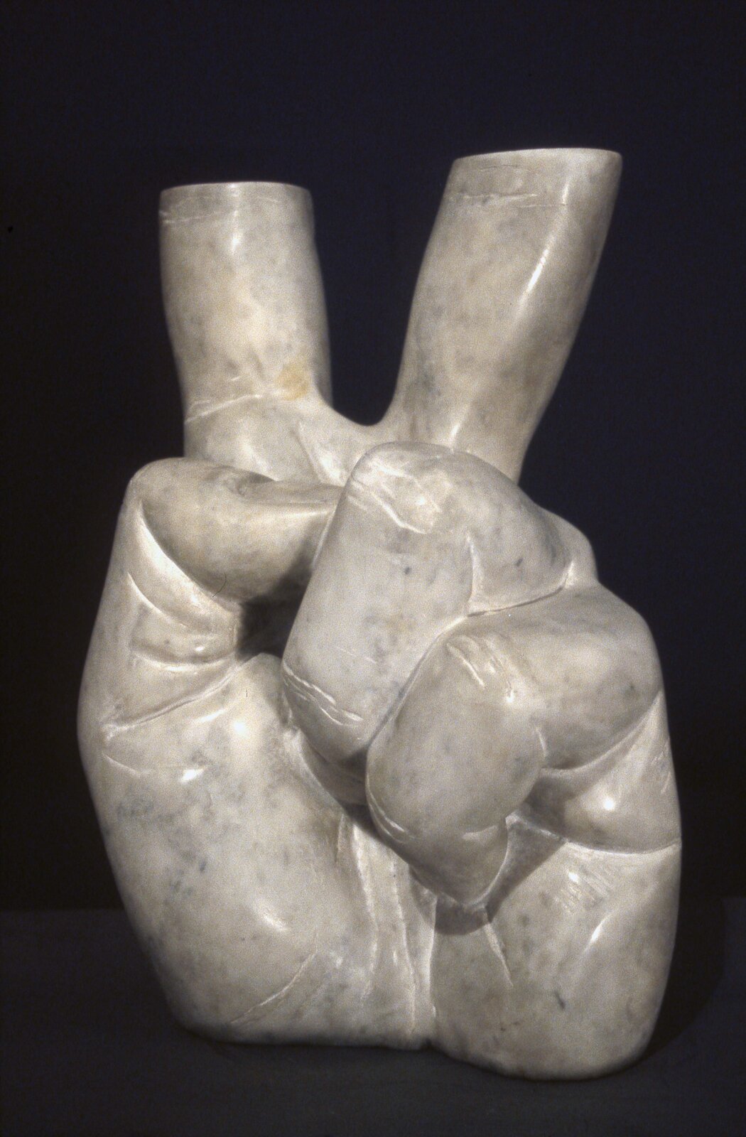 Fotografia przedstawia rzeźbę autorstwa Krzysztofa Bednarskiego, pod tytułem: „Victoria‑Victoria”. Rzeźba przedstawia dłoń z palcami, ułożonymi w znak wiktorii. Palce -środkowy oraz wskazujący są ucięte – brakuje w nich ostatnich, dwóch paliczków. Rzeźba jest koloru szarego. Tło kompozycji jest czarne.