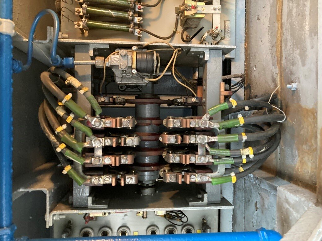 Zdjęcie przedstawia nawrotnik pe er trzysta sześć. Widoczny jest od boku, tak że można w nim zauważyć poszczególne elementy mechanizmu nawrotnika. Na środku widoczny jest wał z zamocowanymi do niego stycznikami i krzywkami. Na górze widać cylinder napędu pneumatycznego oraz elektrozawór. 