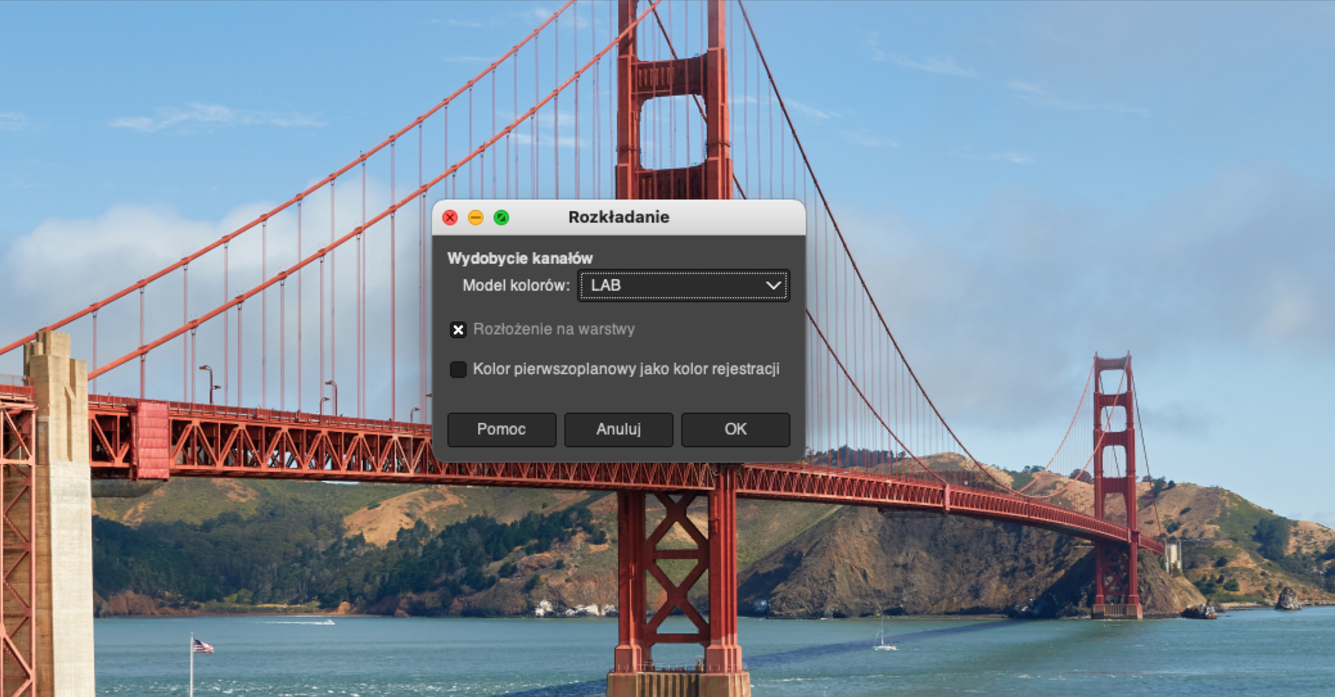 Ilustracja przedstawia wycinek okna w programie GIMP, a wewnątrz niego czerwony most Golden Gate. Na tle fotografii widać niewielkie okno zatytułowane Rozkładanie. W oknie w pierwszej linijce widnieje napis: Wydobycie kanałów, w drugiej Model kolorów i wybrana opcja LAB, w trzeciej linijce zaznaczona krzyżykiem opcja: Rozłożenie na warstwy i odznaczona opcja: Kolor pierwszoplanowy jako kolor rejestracji. Na dole okna widnieją trzy przyciski: Pomoc, Anuluj i OK.