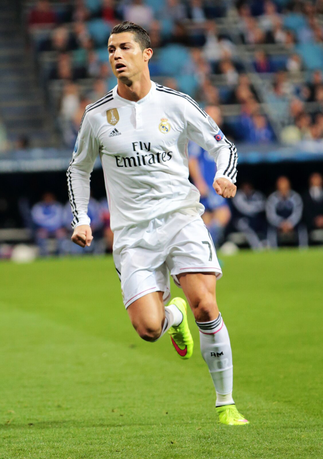 Na zdjęciu został przedstawiony Cristiano Ronaldo. Mężczyzna ma czarne włosy. Są zaczesane gładko do tyłu. Ma otwarte delikatnie usta. Patrzy w prawą stronę.  Jest ubrany w białą koszulkę z długim rękawem. Ma czarne trzy paski na rękawach. Z przodu na bluzce, na środku znajduje się napis: „Fly  emirates”. Po prawej stronie jest logo firmy Adidas. Powyżej został umieszczony złoty znaczek, gdzie znajduje się napis Fifa. Po lewej stronie jest herb klubu. Piłkarz ma krótkie białe spodenki oraz białe getry z czarnymi prążkami u góry. Na stopach ma jaskrawe korki z czerwonym logiem Nike. Piłkarz ma zaciśnięte pięści u obu rąk. Prawa noga jest zgięta i uniesiona do góry. Stoi na lewej nodze. Biegnie po zielonej murawie. W tle są rozmyte trybuny sportowe.