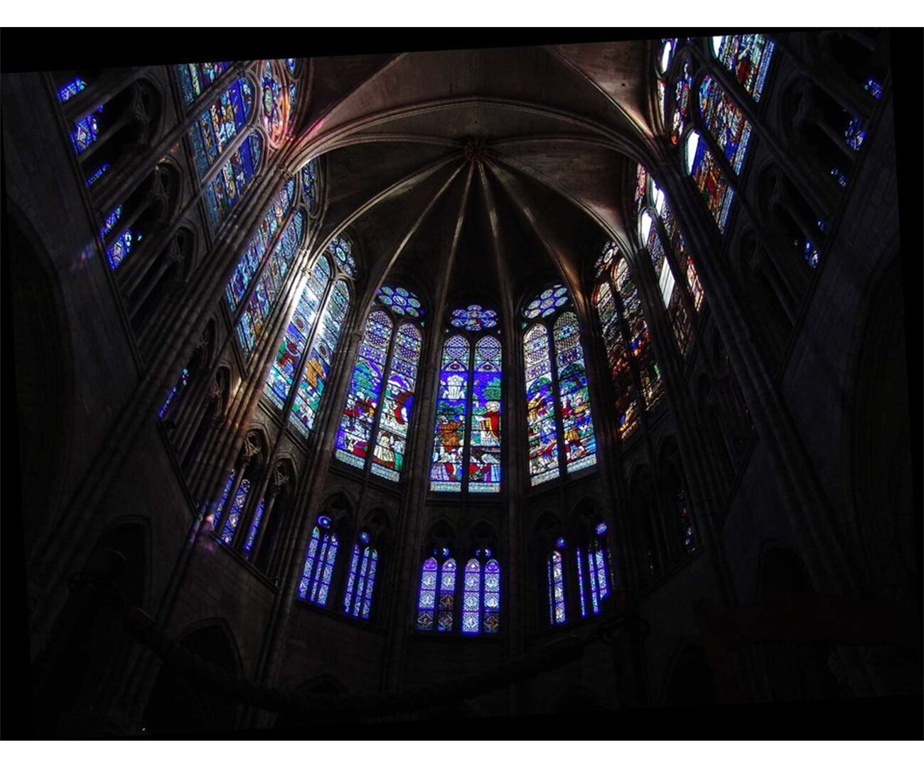 Fotografia barwna przedstawiająca kościół Saint Denis w 13 wieku. Widać wewnętrzną stronę witraży zdobiących sufit. Kolorowe okienka przedstawiają różne scenki.