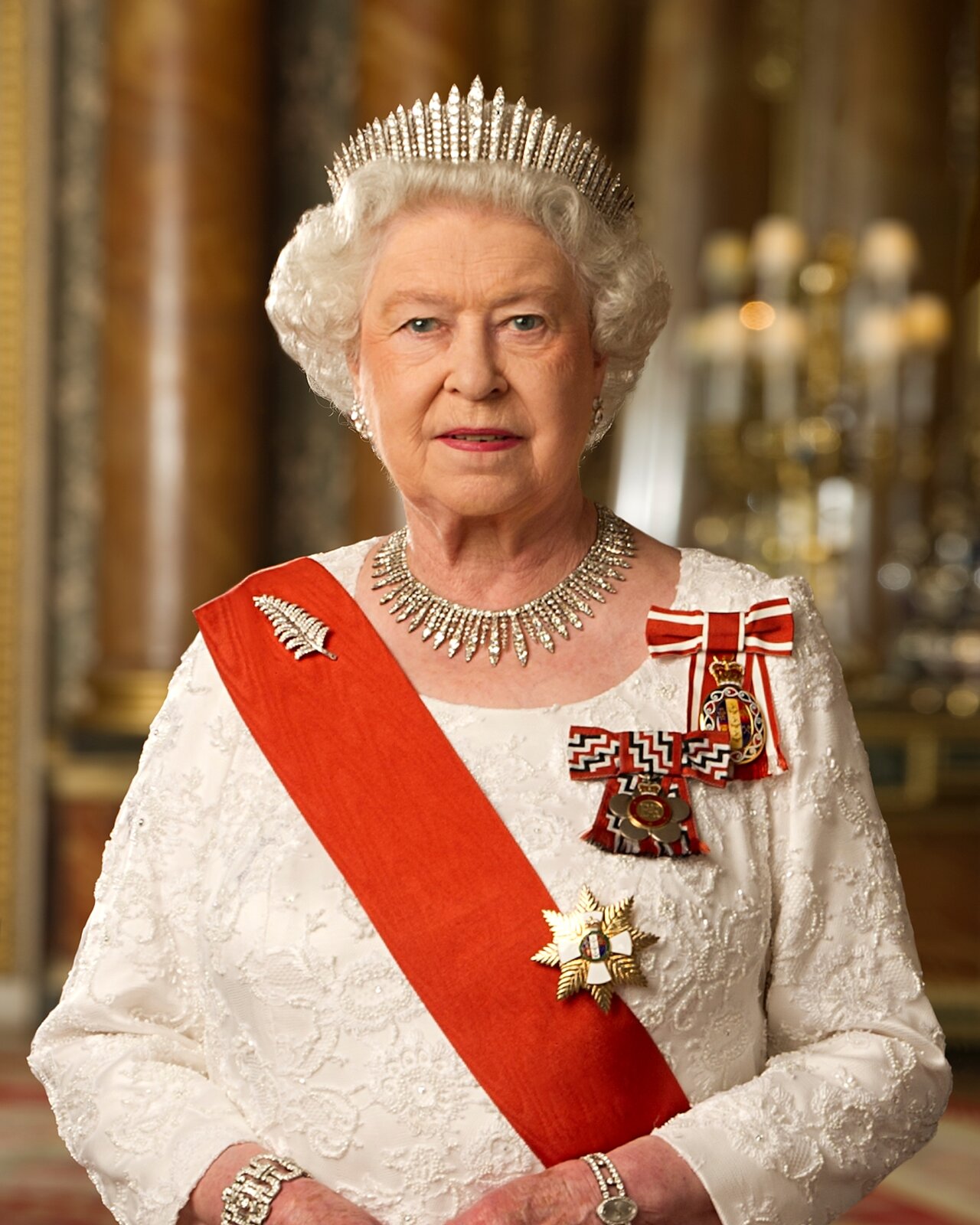 Zdjęcie przedstawia starszą, siwowłosą kobietę. Jest ubrana w białą suknię, przez prawie ramię ma przewieszoną szeroką, czerwoną szarfę. Na lewej piersi ma przypięte trzy odznaczenia. Na głowie ma koronę, a na szyi diadem.