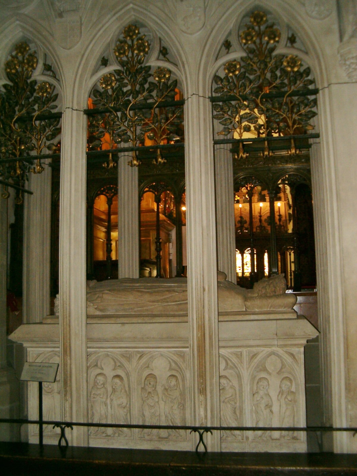 Na zdjęciu za kolumnami widać biały, kamienny grobowiec. Na ścianach grobowca wyrzeźbione są postaci. Na płycie leży kamienna postać w długiej szacie z rękami złączonymi na piersiach. Pod głową ma kamienną poduszkę.