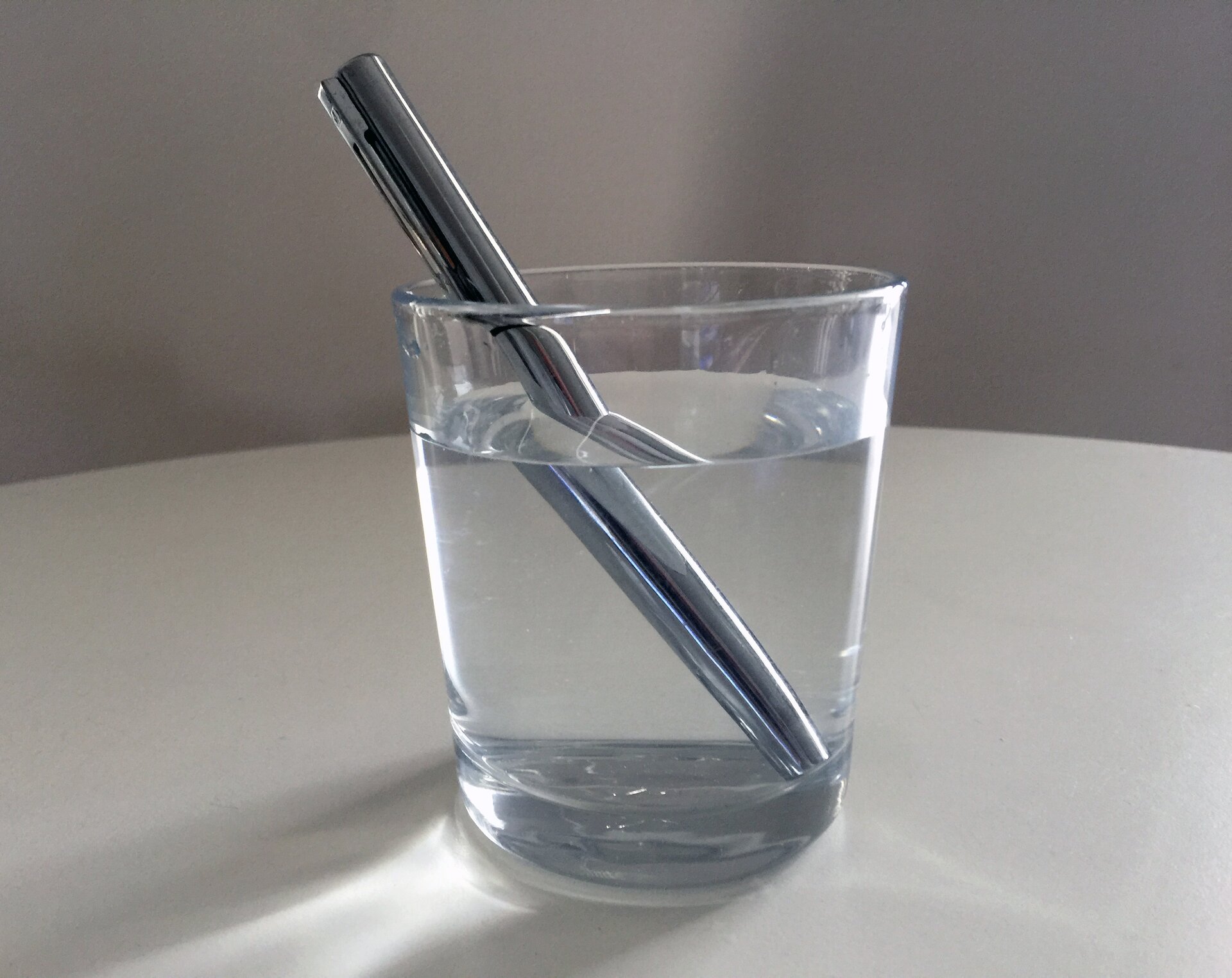 Rys. a. Zdjęcie poglądowe przedstawia metalowy długopis zanurzony w szklance wody. Zdjęcie ilustruje załamanie światła na granicy ośrodków.