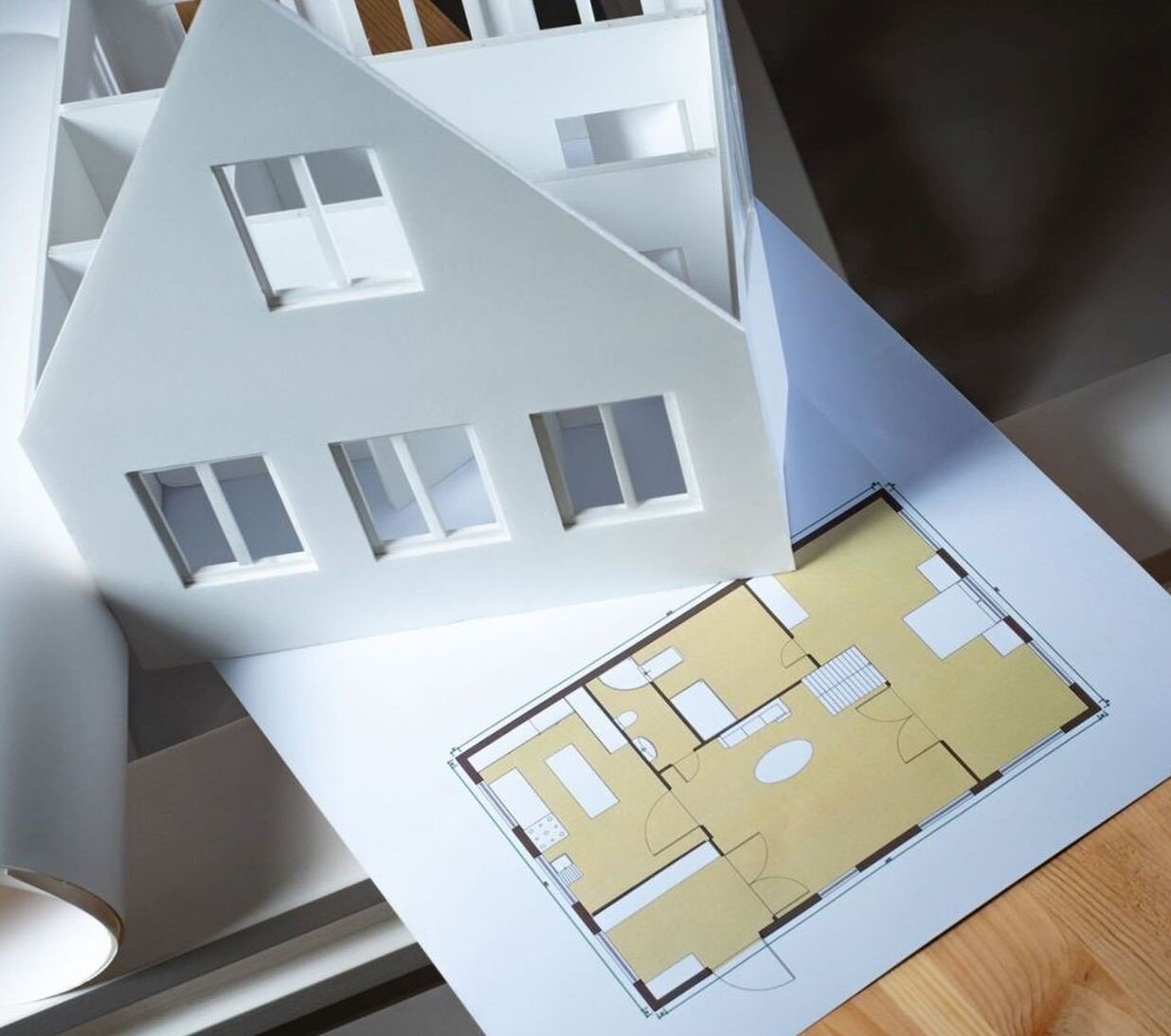 Fotografia przedstawia model budynku jednorodzinnego wykonany z kartonu oraz jego plan (rysunek architektoniczny), leżące na stole .