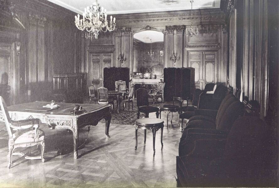 Zdjęcie przedstawia wnętrze dużej, pałacowej sali. Stoi tu duże, bogato rzeźbione biurko z fotelem. Są także kanapy i fotele, a także stół z krzesłami. Ściany sali są wykończone marmurem, lustrami.