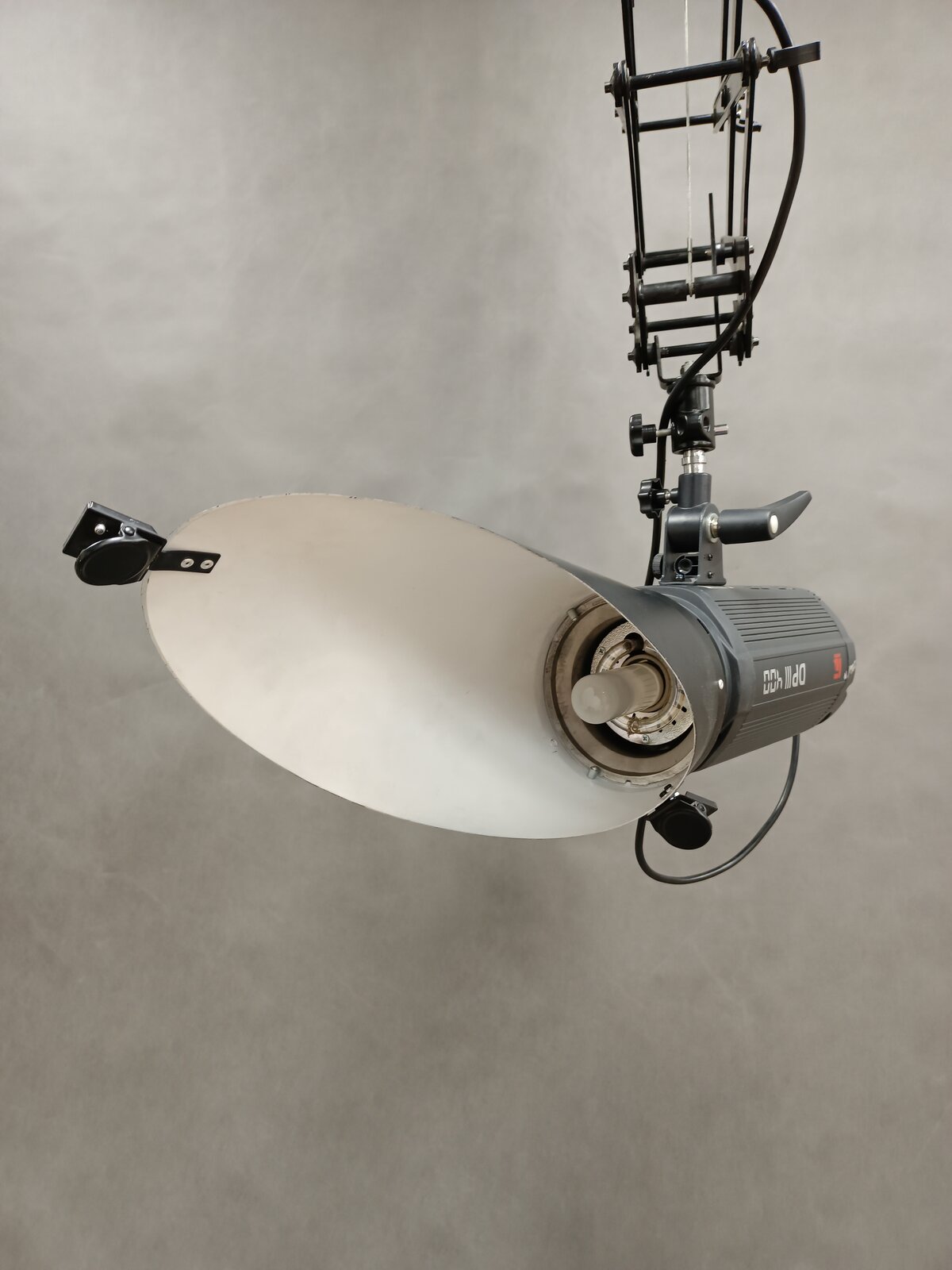Zdjęcie przedstawia lampę studyjną z nałożoną czaszą, która jest podwieszona do wysięgnika, lampa z czaszą jest ułożona tak, że widać wnętrze czaszy i żarówkę.