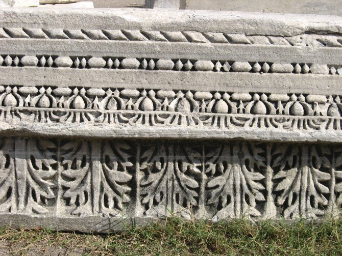 Zdjęcie przedstawia kamień z dekoracyjnym wzorem (tzw. fryzem), biegnącym w kilku rzędach; pierwszy, szeroki w formie listków, następne roślinne i geometryczne.