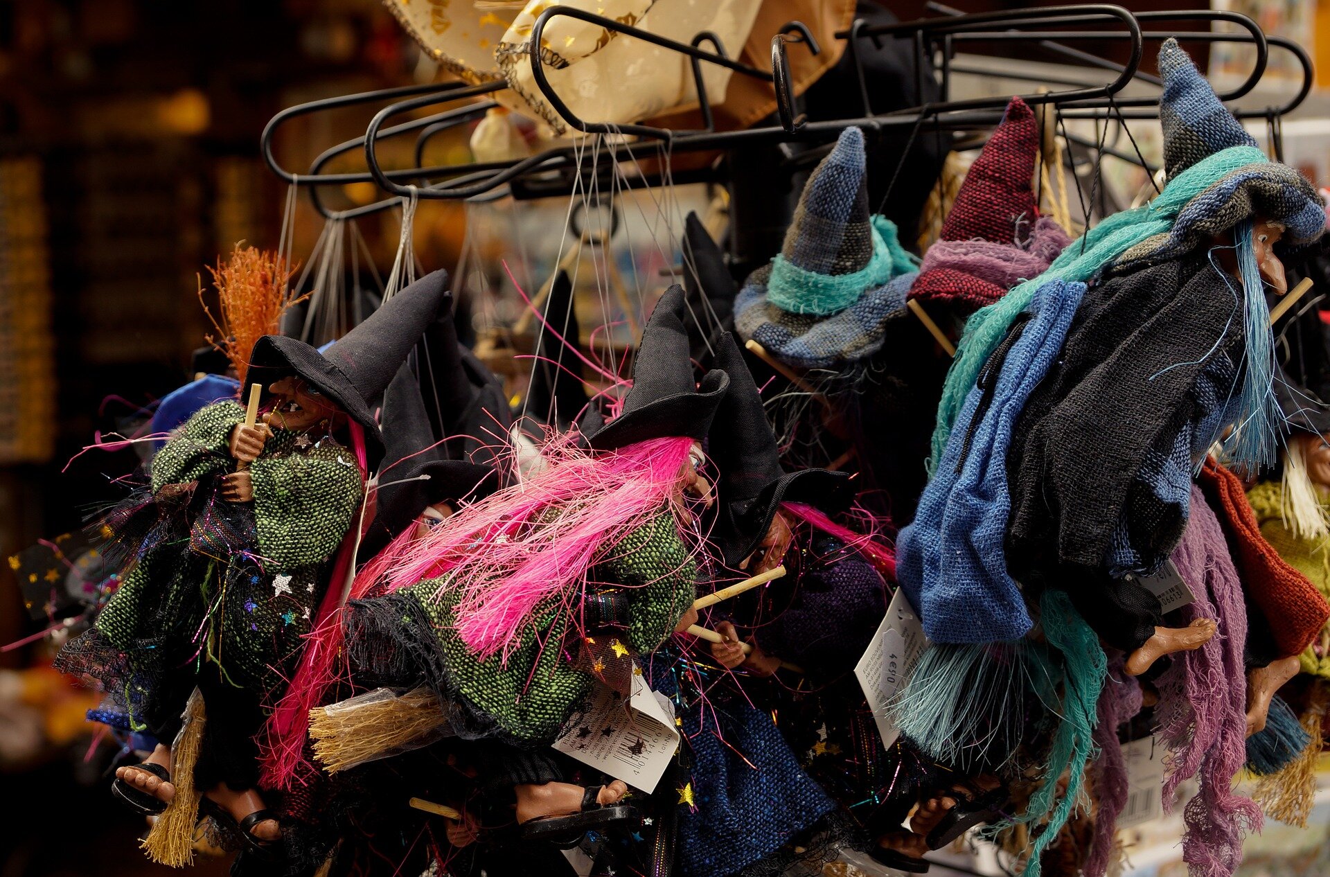 Zdjęcie przedstawia wnętrze sklepu z zabawkami. Na wieszakach wiszą szmaciane figurki czarownic na drewnianych miotłach i w stożkowatych, czarnych kapeluszach.