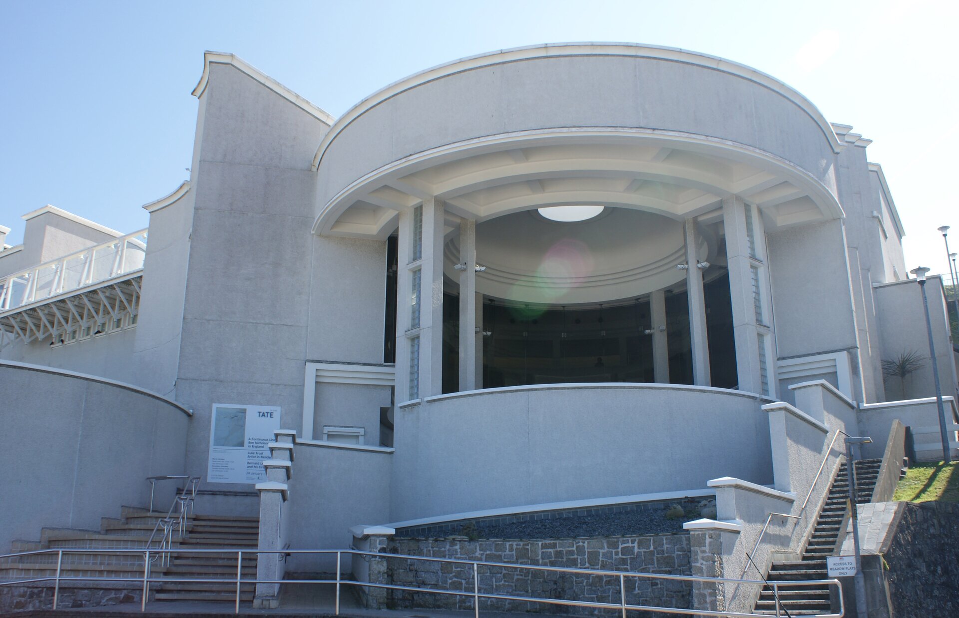 Na zdjęciu przedstawiono wejście do budynku, Jest to konstrukcja w kształcie półokręgu, do której prowadzą schody z prawej i lewej strony. Fasada jest biała. Wewnątrz tego półokrągłego elementu, znajduje się dach z oculusem.