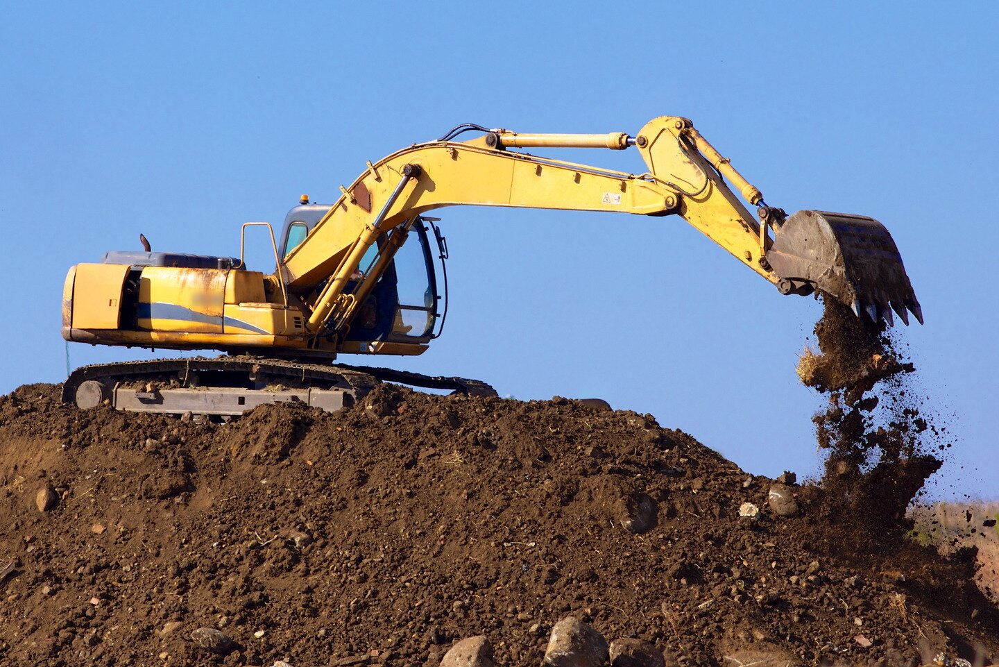 Ilustracja przedstawia żółtą koparkę gąsienicową, która kopie w ziemi. 