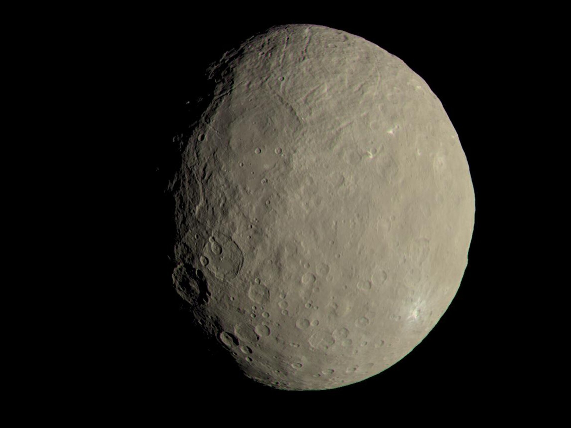 Rys. 1. Zdjęcie poglądowe przedstawia planetę Ceres. Ceres ma rozmiary 976 km razy 909 km oraz masę 10²¹ kg (to prawie 100 razy mniej niż masa ziemskiego Księżyca). Rok na Ceres trwa 4,6 roku ziemskiego, a dzień na Ceres (czyli pełny obrót wokół własnej osi) trwa 9 h. Astronomowie czasami nazywają ją embrionem planetarnym, dlatego, że jest utworzona z najbardziej pierwotnej materii, z której powstawał Układ Słoneczny. Ceres jest pierwszą planetą karłowatą, do której dotarła sonda kosmiczna w celu zbadania struktury jej powierzchni. Była to sonda Dawn, która doleciała do Ceres w marcu 2015 roku. Sonda znajdowała się na orbicie wokół Ceres przez wiele miesięcy, dzięki czemu wykonała wiele zdjęć i pomiarów z każdej strony tej planety karłowatej. Dzięki badaniom tej sondy znamy dokładnie strukturę powierzchni Ceres oraz jej budowę.