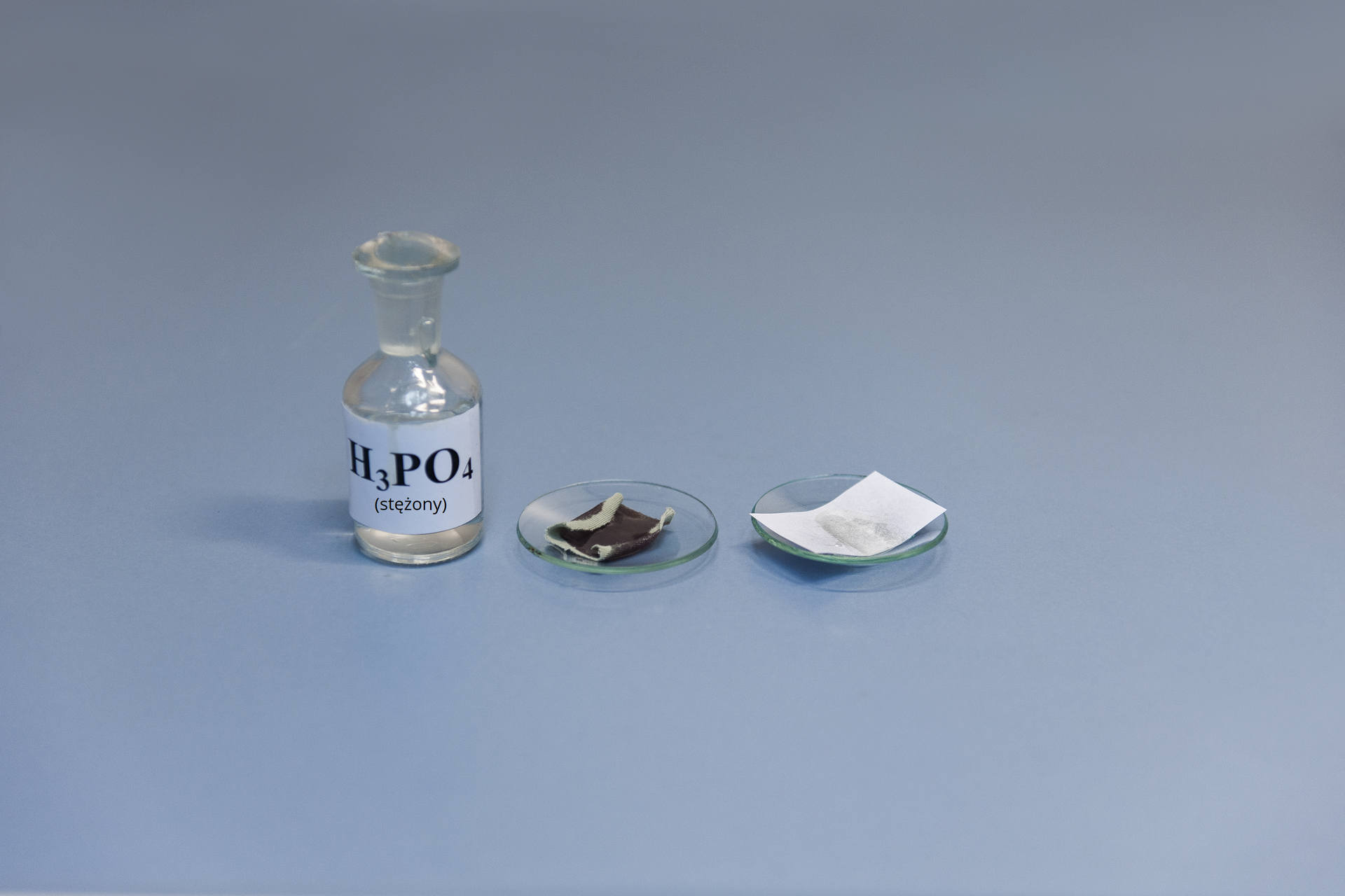 Drugie zdjęcie w galerii przedstawia stan końcowy tego samego eksperymentu, co na pierwszej ilustracji. Papier jest silnie poczerniały i pozginany na końcach, natomiast tkanina pozostaje cała.