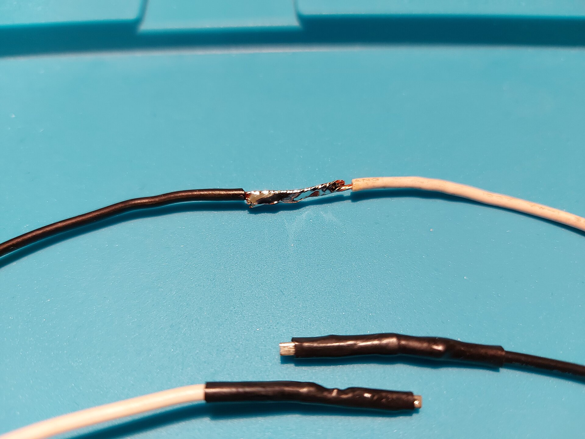 Zdjęcie przedstawia 4 przewody z czego 2 z usuniętą izolacją tym samym odsłaniając miedziane wnętrze oraz 2 z taśmą izolacyjną na końcach. W przypadku odsłoniętych przewodów, kable zlutowano na siebie, przykładając je po całej długości do siebie.