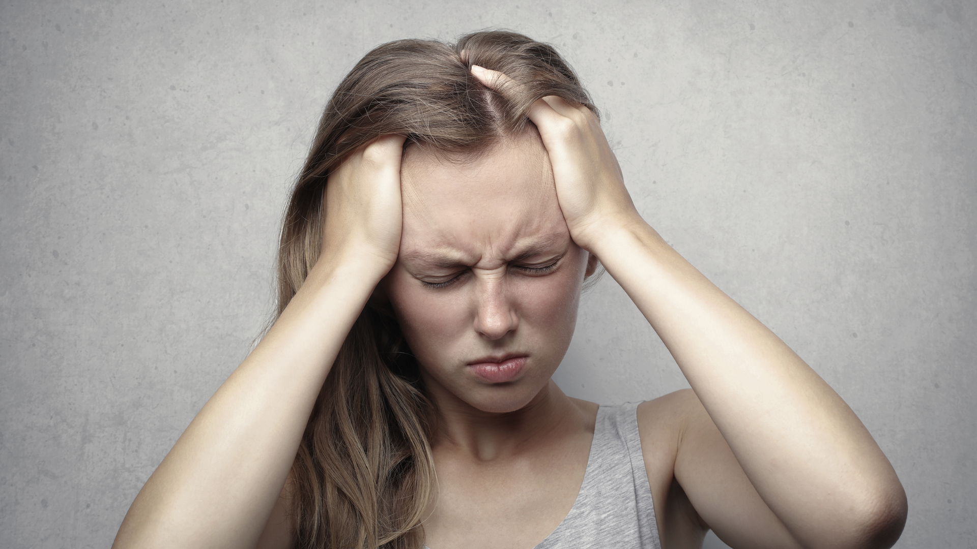 Zdjęcie kobiety trzymającej się za głowę. Na jej twarzy widoczny jest grymas bólu.