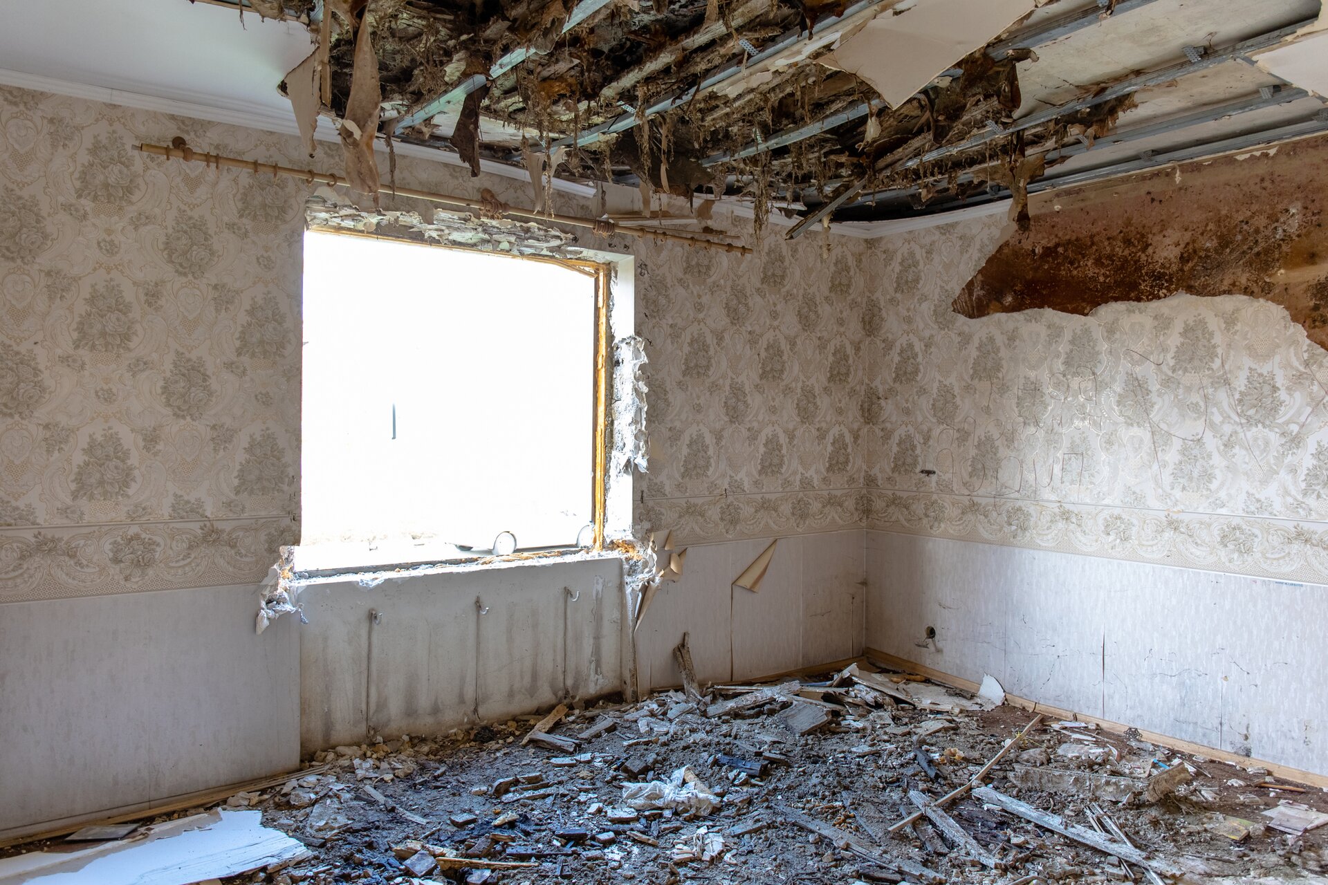 Zdjęcie przedstawia uszkodzenia izolacji termicznej stropów. Widoczny jest pęknięty sufit. Widać profile, do których był on przymocowany. Z uszkodzenia zwisają resztki izolacji.
