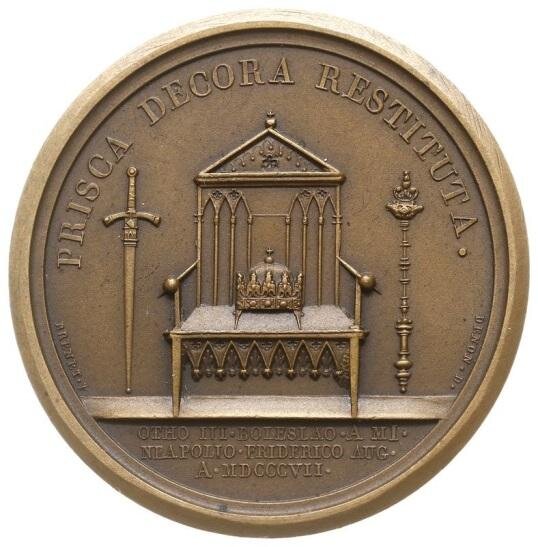 Zdjęcie przedstawia rewers medalu. Pośrodku znajduje się tron, na którym leży królewska korona. Po prawej stronie tronu stoi pionowo miecz, po lewej berło królewskie.