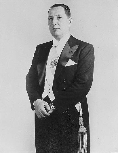 Zdjęcie przedstawia postawnego, dojrzałego mężczyznę we fraku. Mężczyzna jest ciemnowłosy, ma owalną twarz.