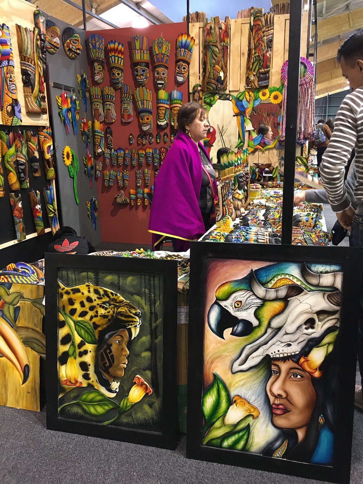 Zdjęcie przedstawia kobietę sprzedającą na stoisku sztukę indiańską. Są to obrazy, drewniane kolorowe maski i inne ozdoby z licznymi motywami roślinnymi i zwierzęcymi.