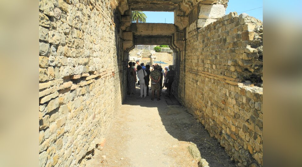 Zdjęcie przedstawia ruiny fragmentu teatru. To niewielki, kamienny korytarz, którym idą turyści.