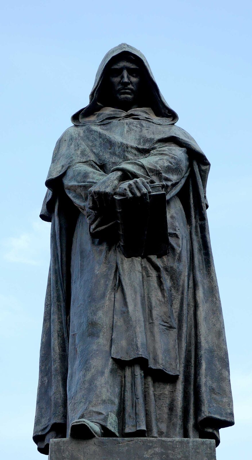 Zdjęcie przedstawia pomnik mężczyzny w długim habicie z kapturem na głowie. W skrzyżowanych rękach trzyma księgę.
