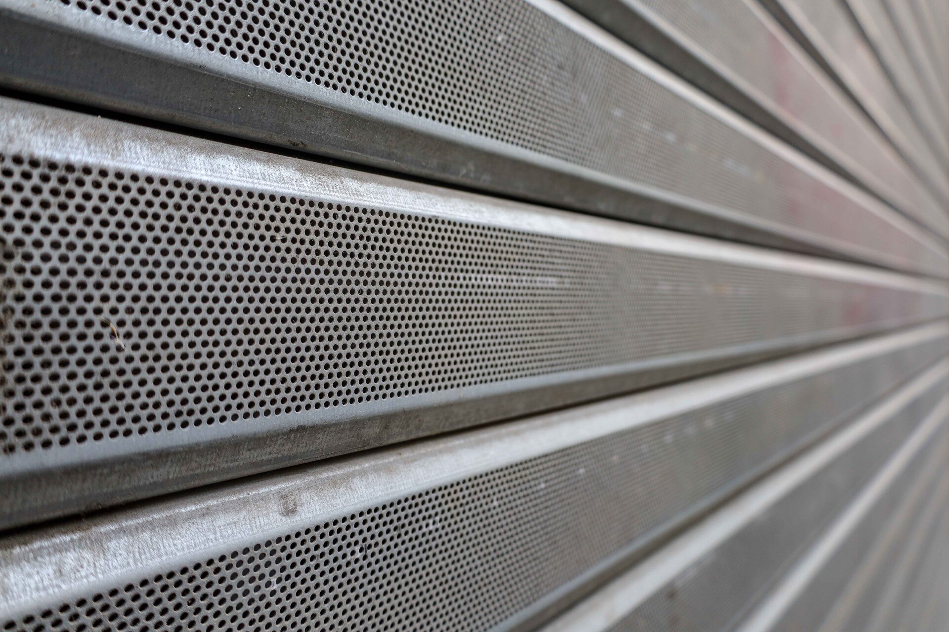 Zdjęcie przedstawia zbliżenie na szary aluminiowy panel o perforowanej strukturze.
