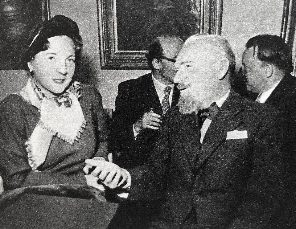 Fotografia przedstawia dwoje siedzących ludzi. Po lewej stronie ukazana jest dojrzała kobieta. Ukazuje prawy półprofil owalnej twarzy. Jej czoło jest gładkie. Ma cienkie brwi i małe oczy. Nos kobiety jest prosty, a usta lekko otwarte. Jest ubrana w sukienkę. Na szyi ma przewiązaną apaszkę. Po lewej stronie siedzi dojrzały mężczyzna. Ma gładko zaczesane, krótkie włosy i wysokie czoło. Jego brwi są cienkie, a czy wąskie. Mężczyzna ma duży nos. Jego wąsy i broda są gęste i krótko ostrzyżone. Ubrany jest w koszulę i marynarkę. Na szyi ma zawiązaną muchę.