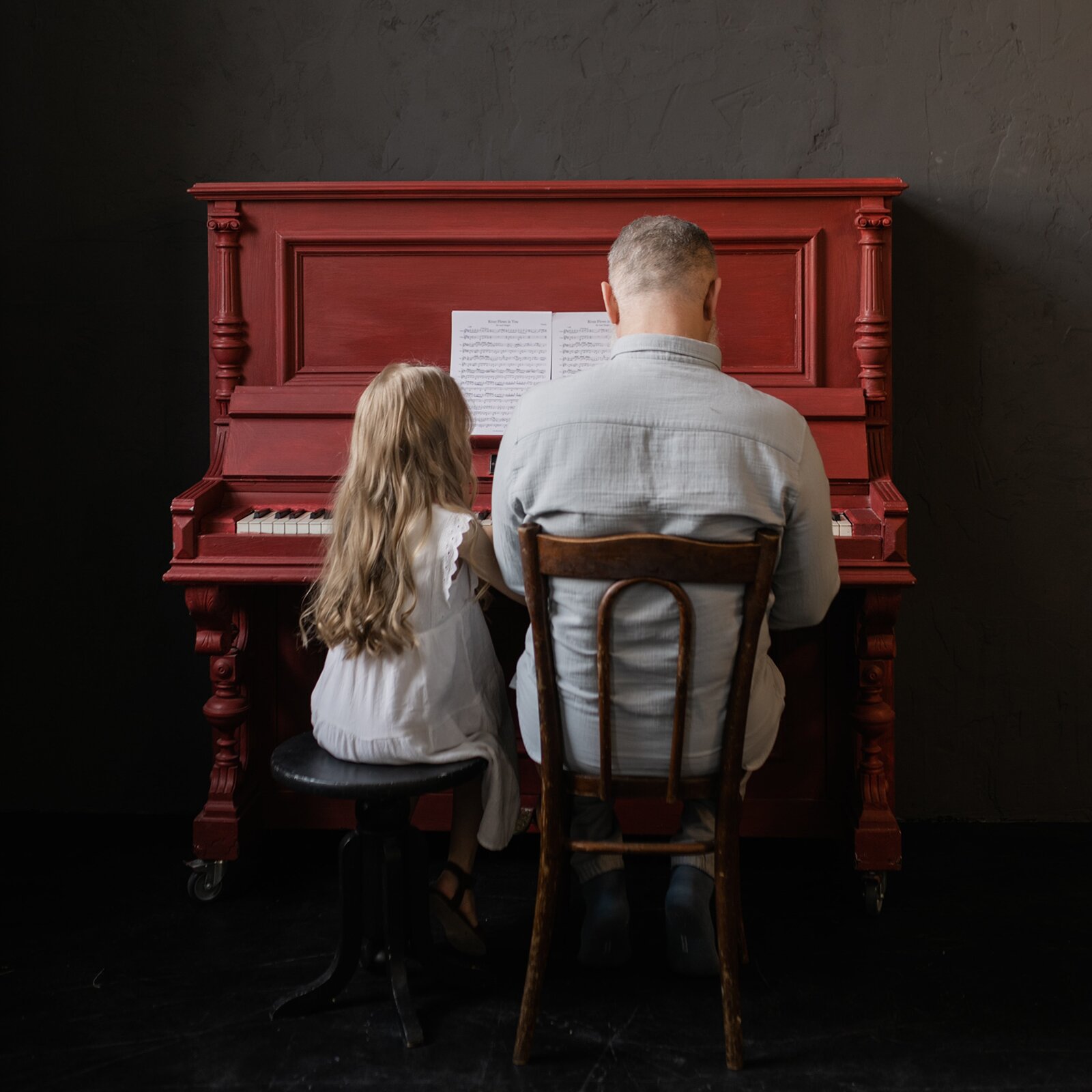Zdjęcie przedstawia pianino, przy którym siedzi mężczyzna i dziewczynka. 