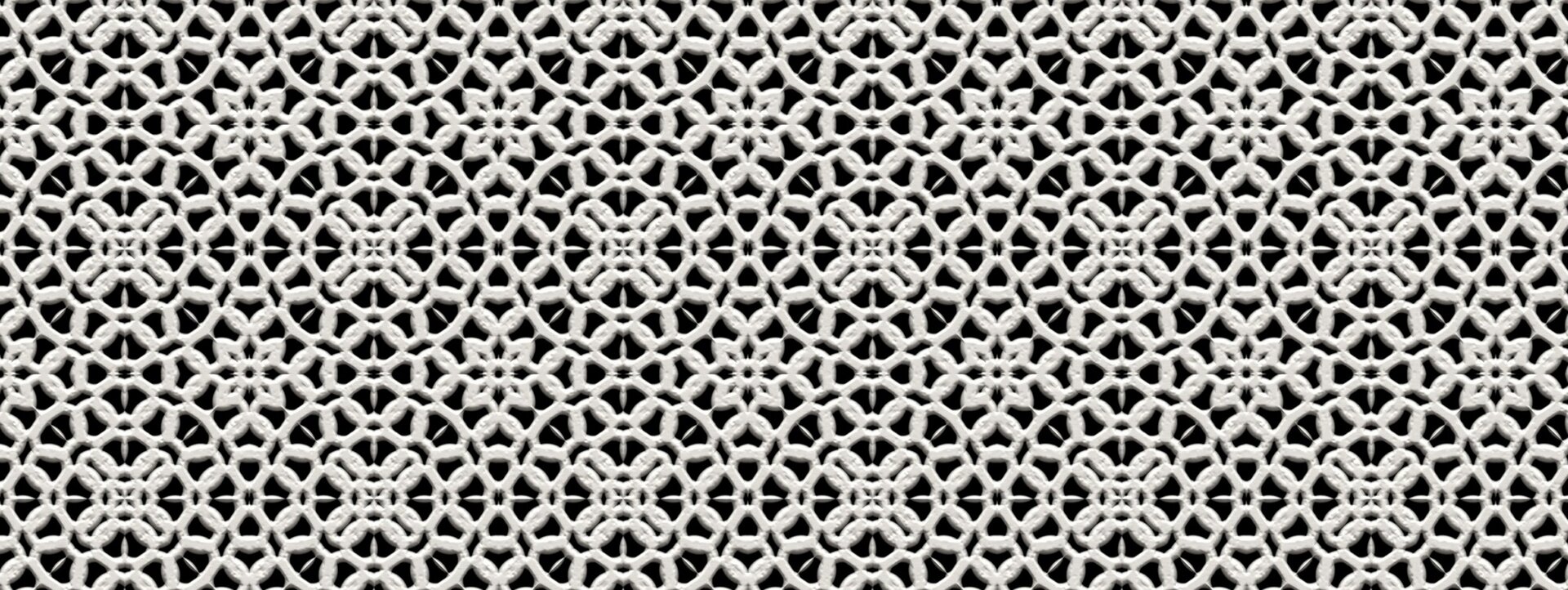 Ilustracja przedstawia fragment białej koronki na czarnym tle. Koronka składa się z rytmicznych, połączonych z sobą wzorów opartych na kolistym kształcie. Wszystkie połączone są czterolistnym kwiatkiem.